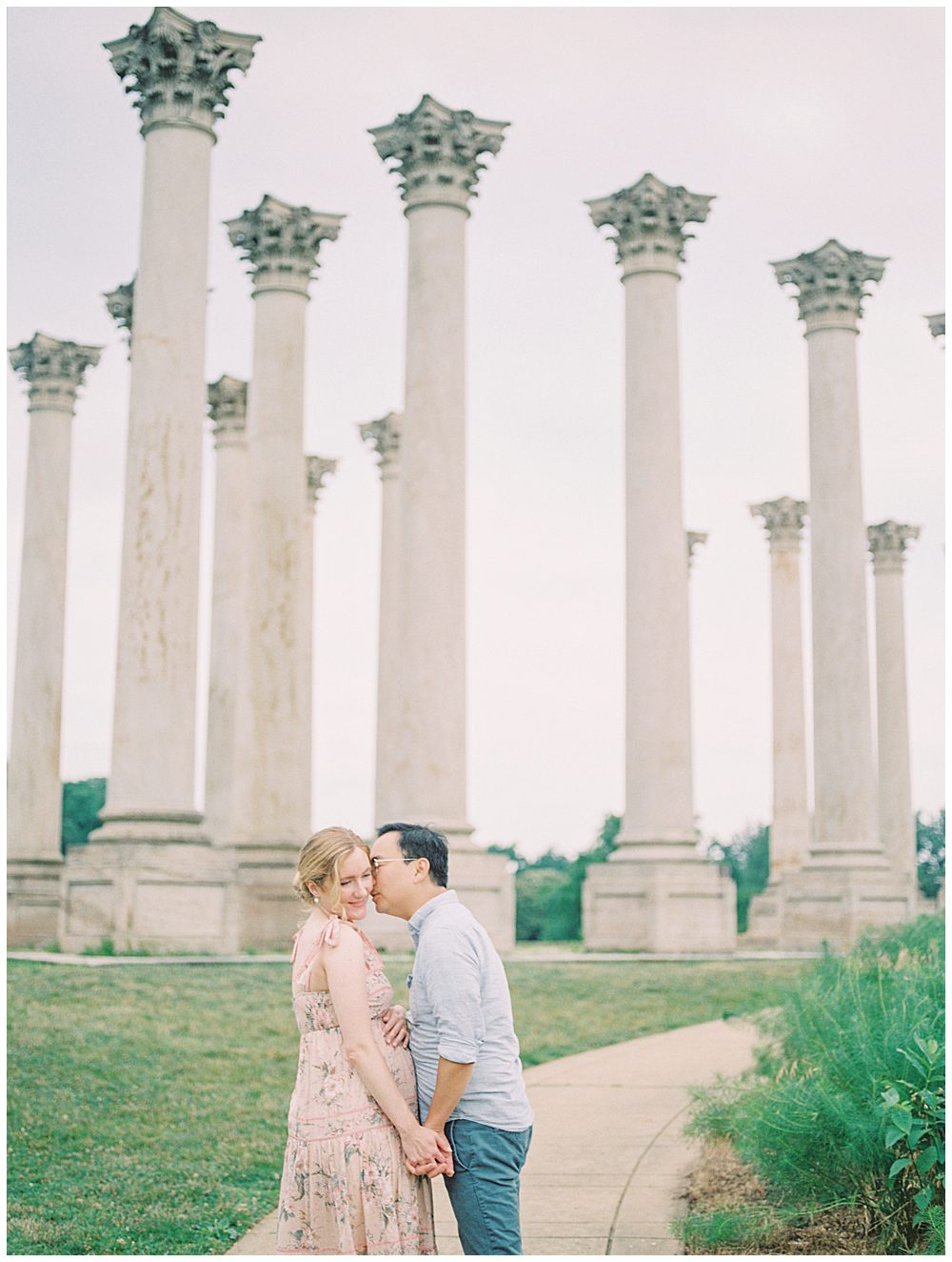 Husband leans over to kiss his wife's cheek during their National Arboretum maternity session.