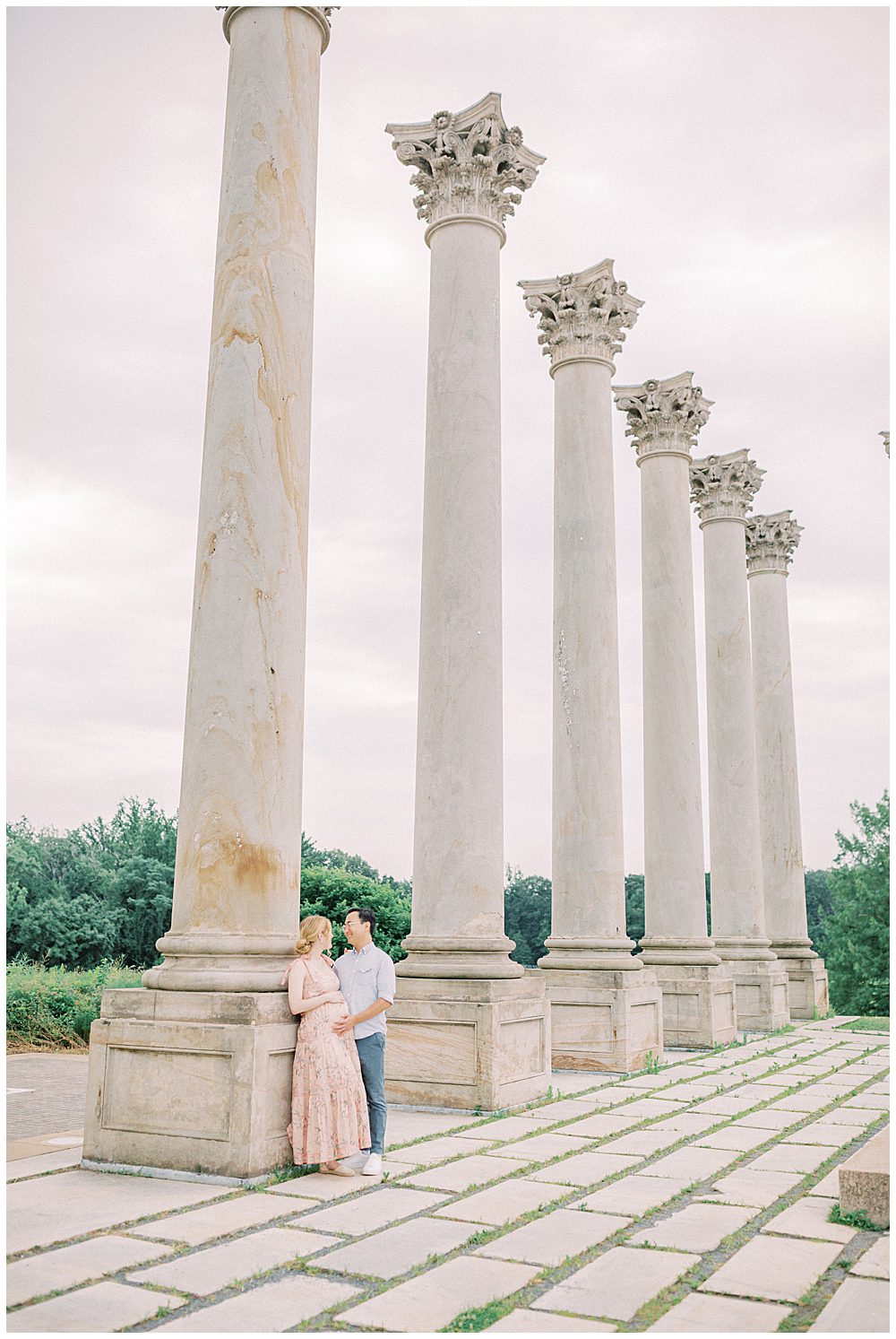 Expecting parents lean against National Arboretum columns looking at one another during their maternity session.