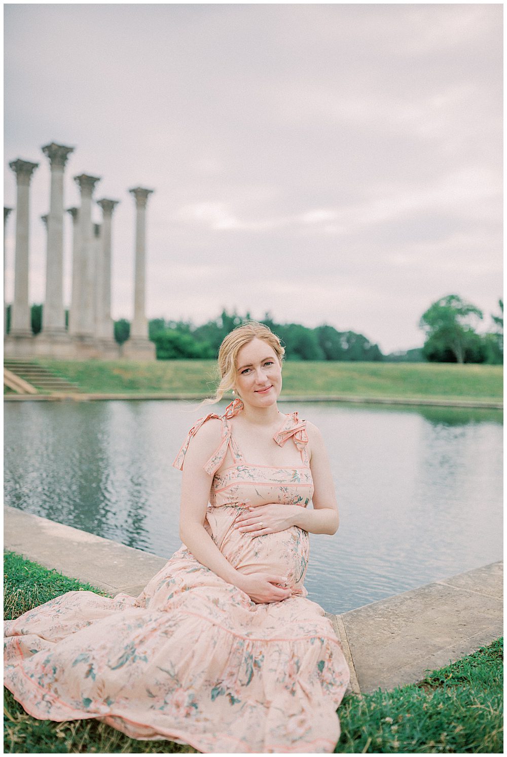 Blonde pregnant mother in pink dress sits in front of pond at the National Arboretum.