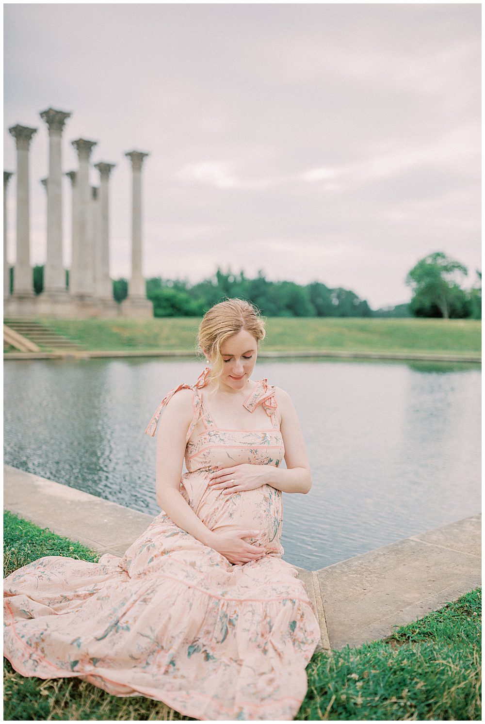 Expecting mother sits in front of National Arboretum pond looking down at her belly during her National Arboretum maternity session.