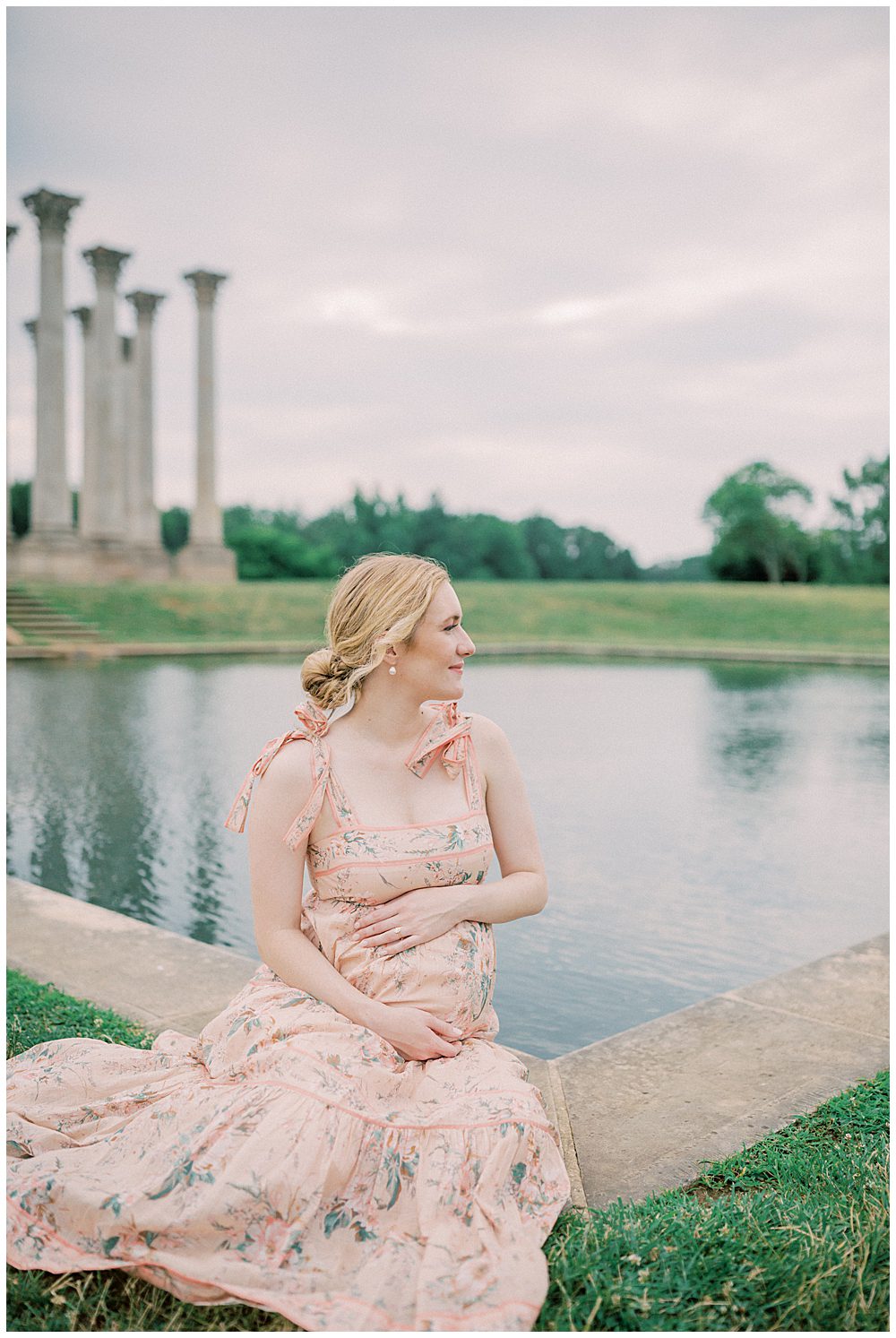 Pregnant mother sits in front of the National Arboretum pond, smiling off into the distance.