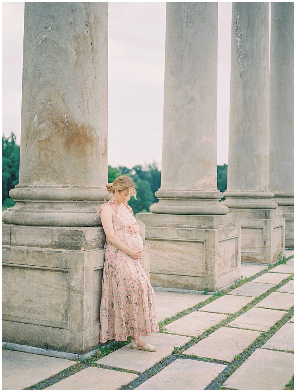 Blonde mother leans against National Arboretum columns during her maternity session in summer.