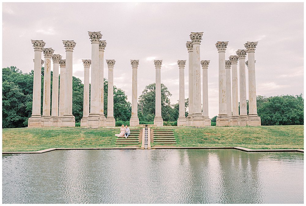 Wide view of husband and wife sitting on steps by the columns at the National Arboretum.