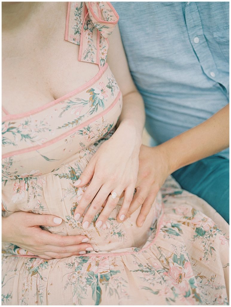 Expecting parents sit while placing their hands on pregnant mother's stomach.