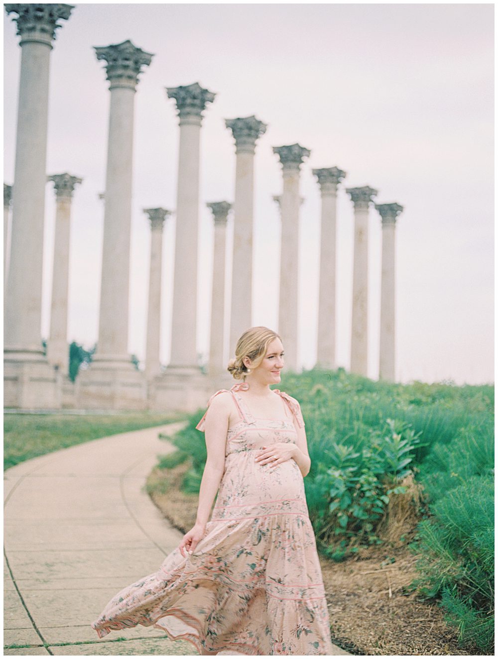 Pregnant mother in pink Zimmerman floral dress walks in front of the columns during her National Arboretum maternity session.