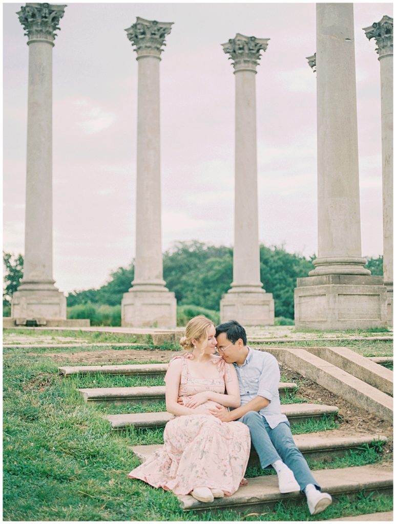 Expecting mother and her husband sit on steps in front of the National Arboretum Columns during their maternity session