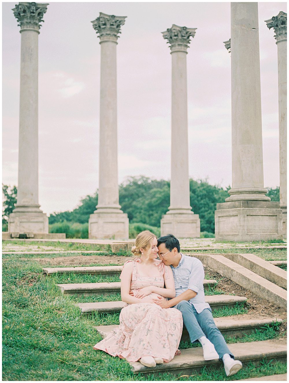 Mother and father sit on steps in front of the columns at the National Arboretum and lean into one another.