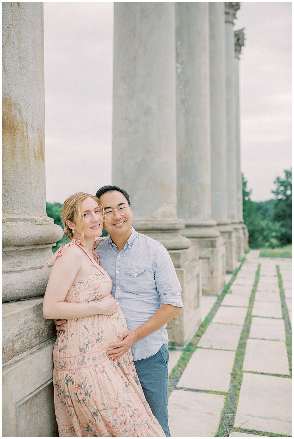 Expecting parents lean against a column at the National Arboretum and smile during their maternity session.
