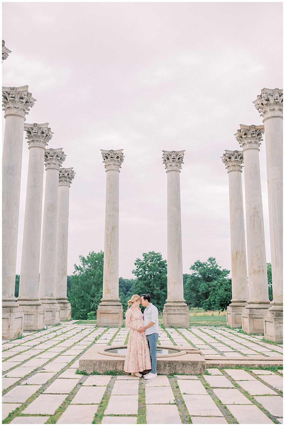 Mother and father stand in the middle of the columns at the National Arboretum facing one another during their maternity session.