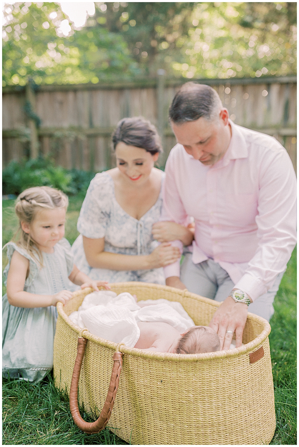 Mother, father, and big sister lean over a Moses basket admiring their new baby during their outdoor newborn session