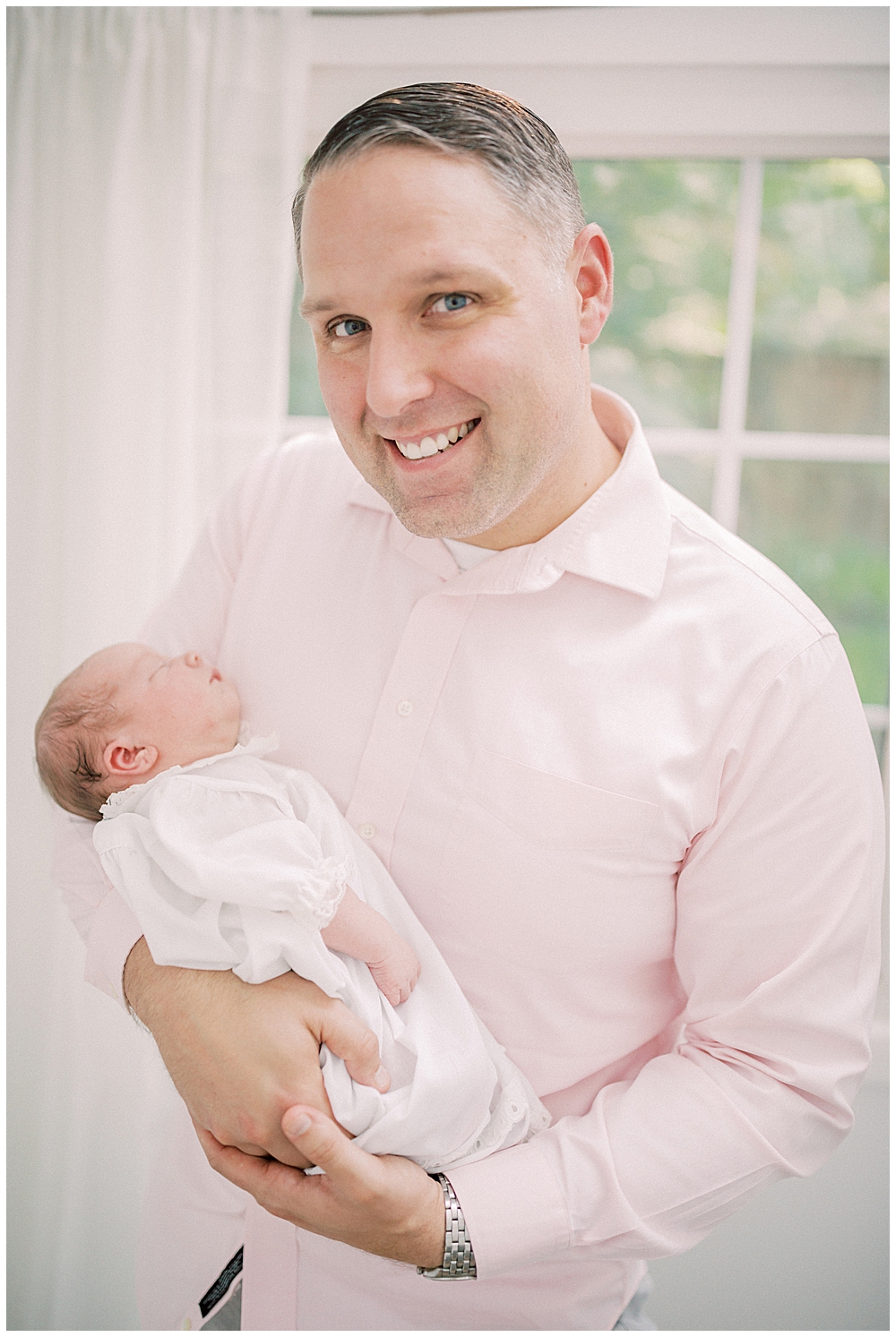 Dad in pink shirt smiles while holding his newborn baby girl