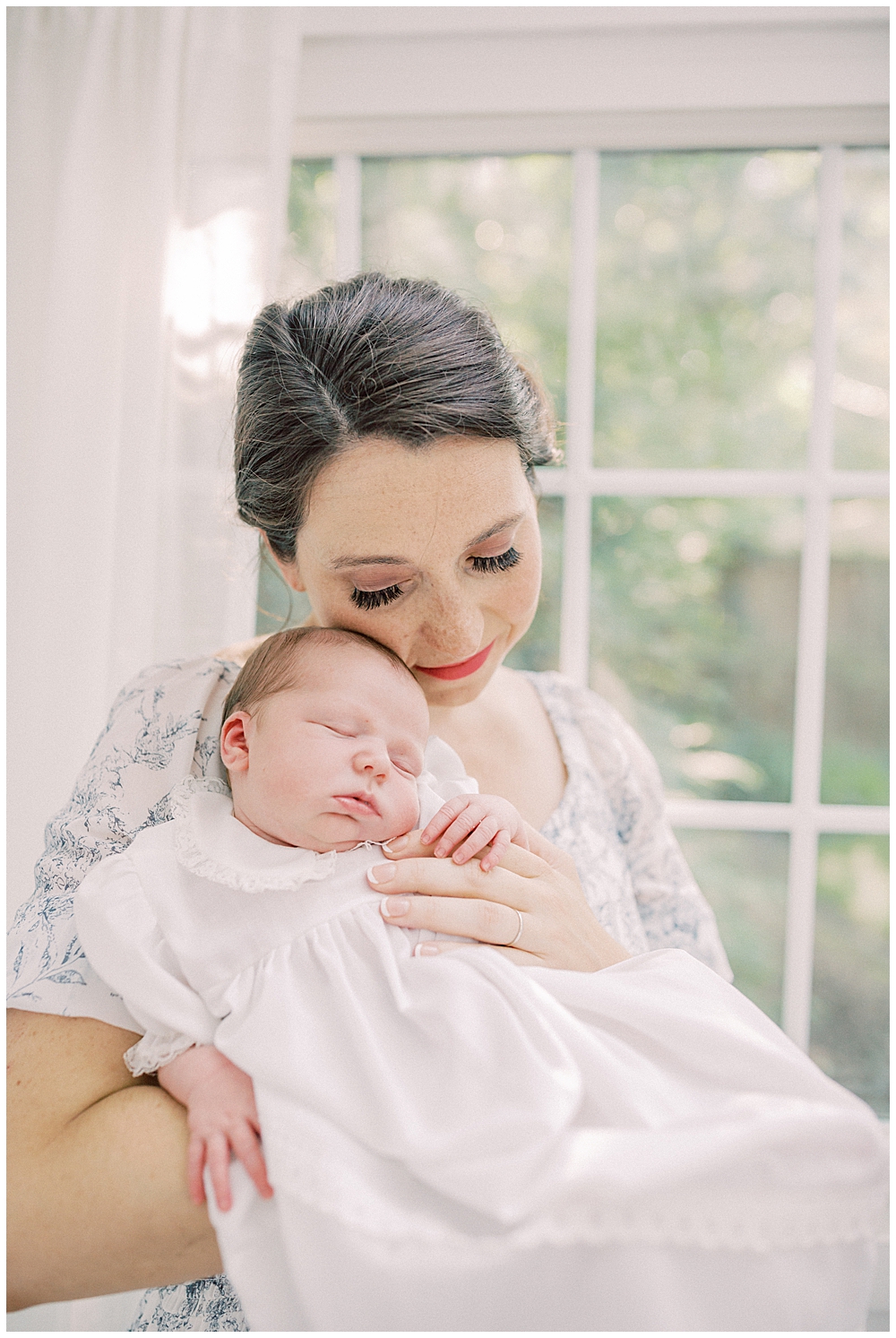 Baby girl held up to her mother's cheek during her studio outdoor newborn session