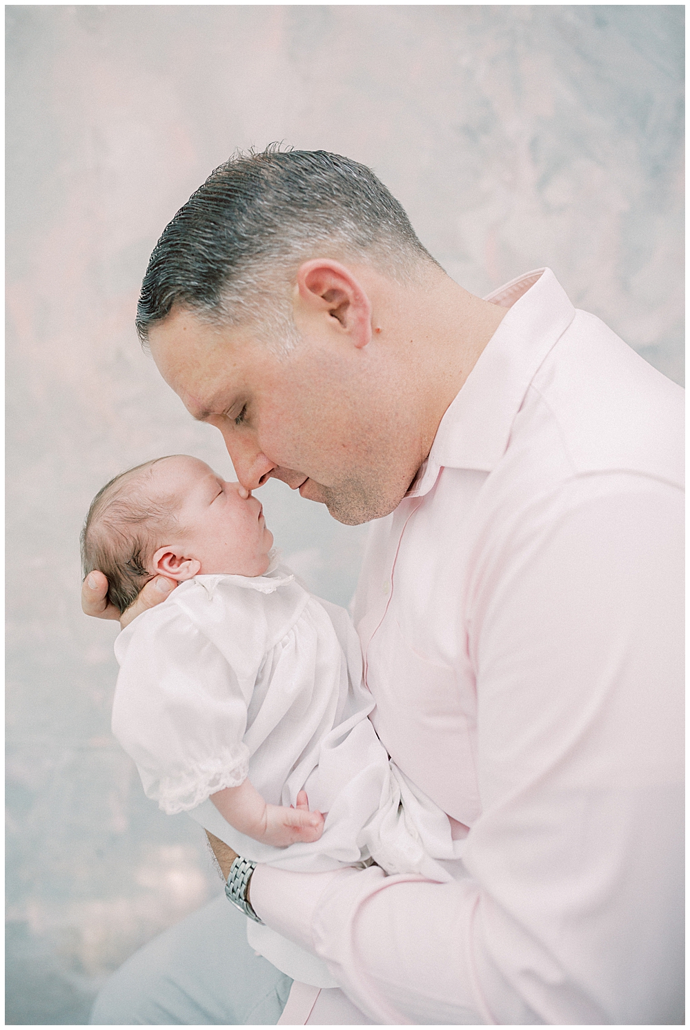 Father holds his newborn daughter up to nuzzle her on the nose