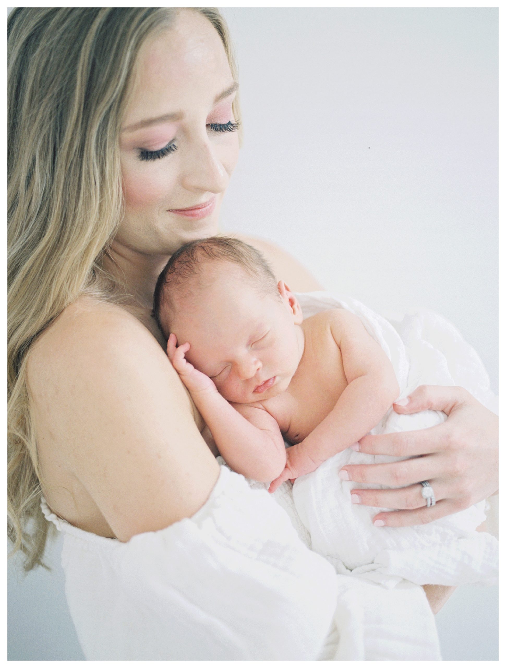Blonde new mother in ivory dress holds newborn baby up to her chest during DC Newborn Session.