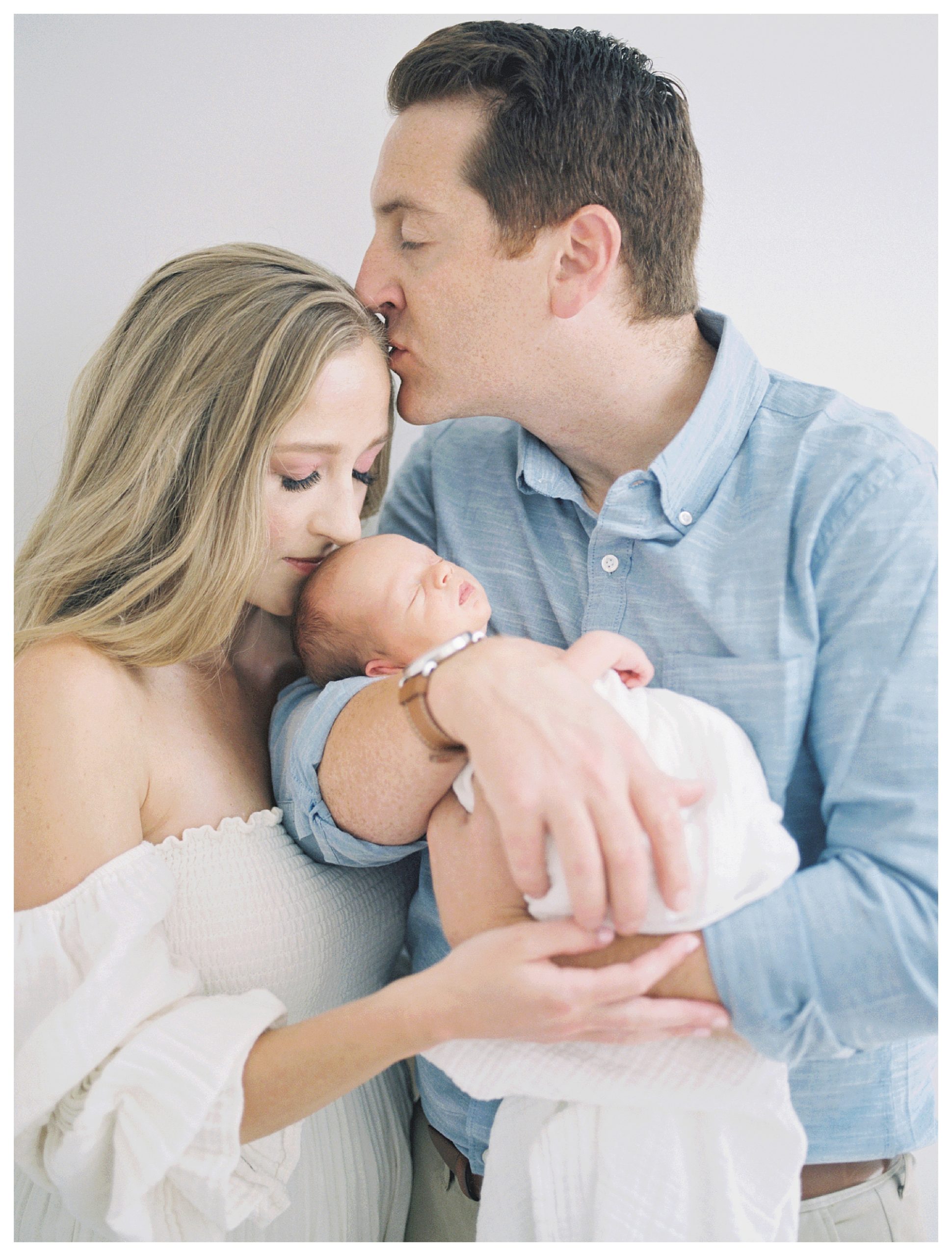 New father kisses his wife's forehead as they hold their newborn baby during their DC newborn session.