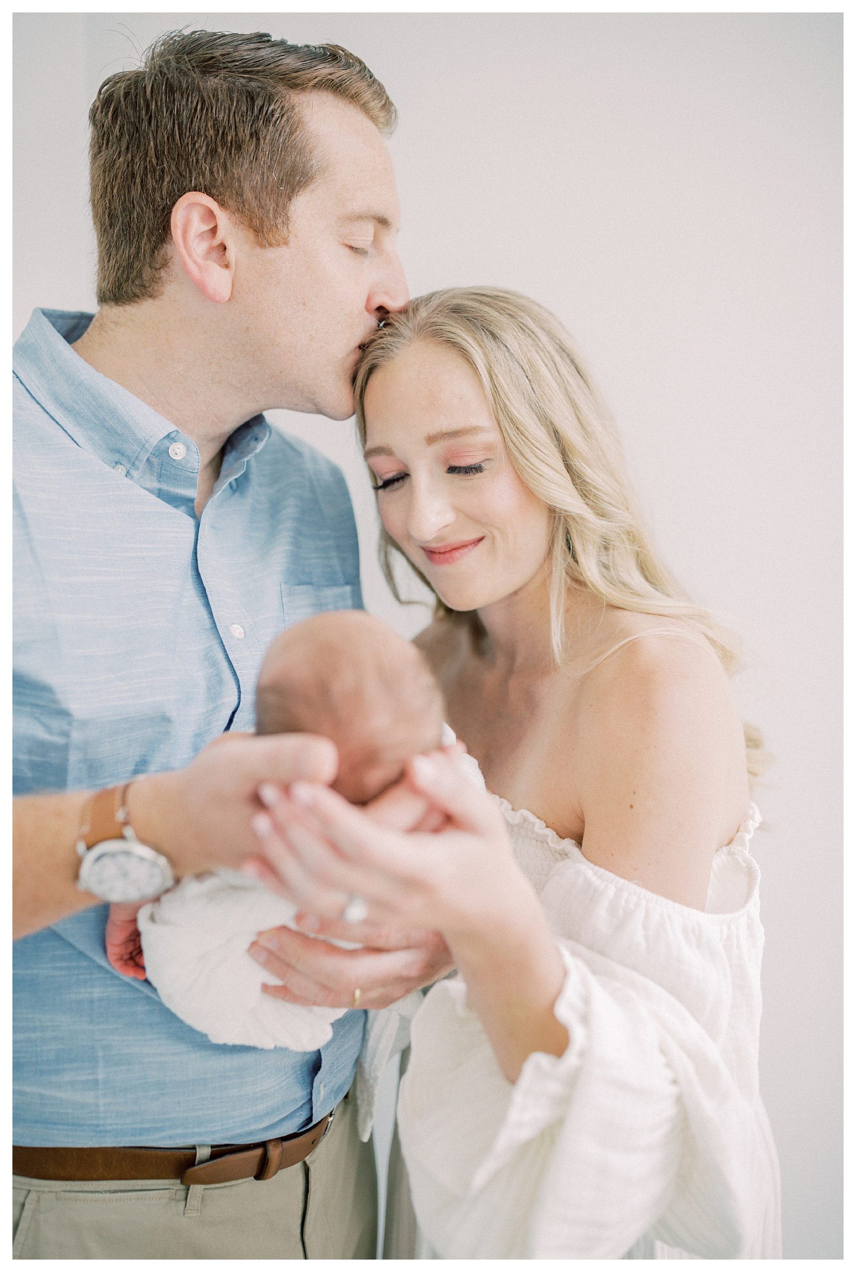 Father kisses his wife's head as they hold their baby during their DC newborn session.