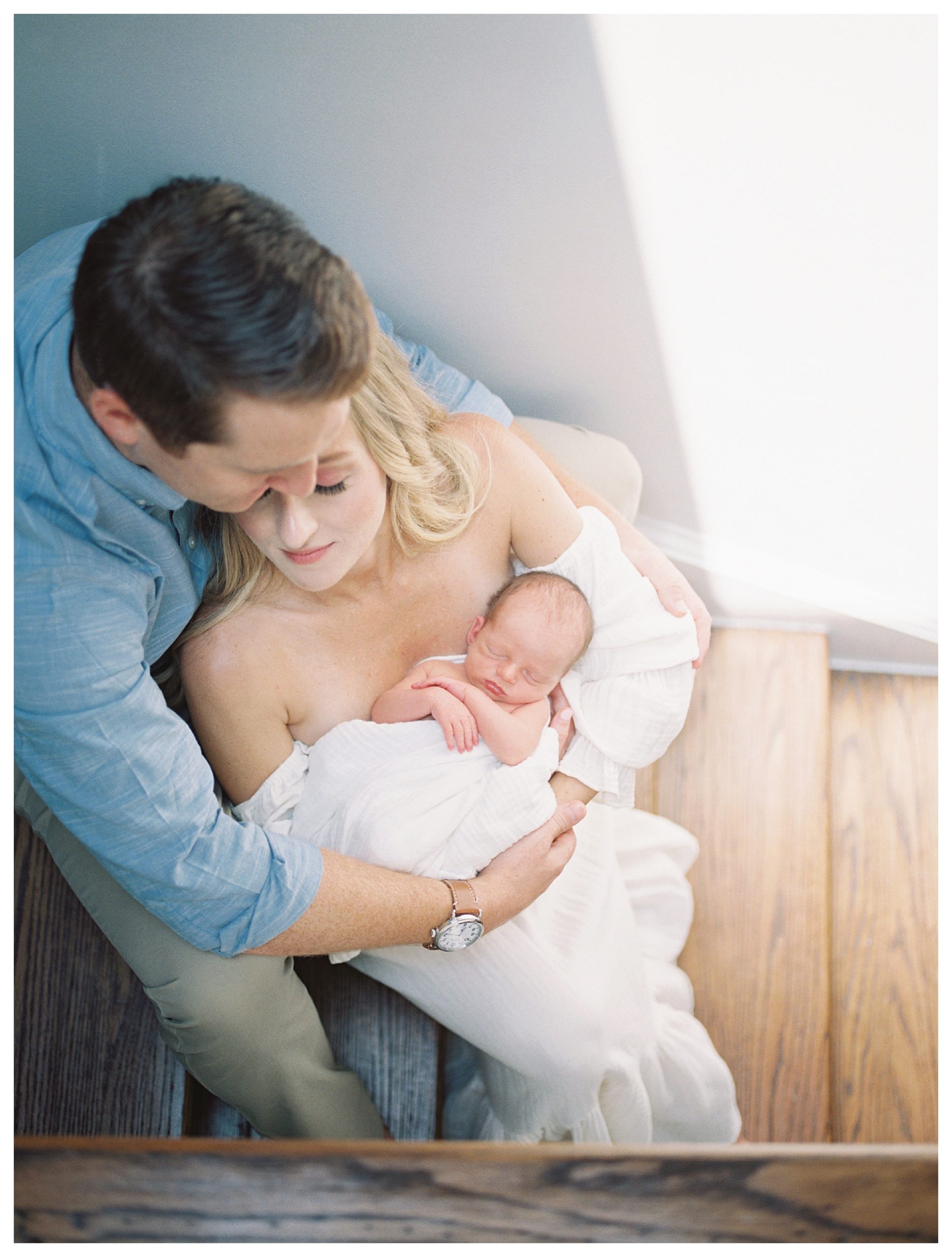 Blonde mother leans into her husband while holding their baby as they sit on their steps during their DC newborn session.