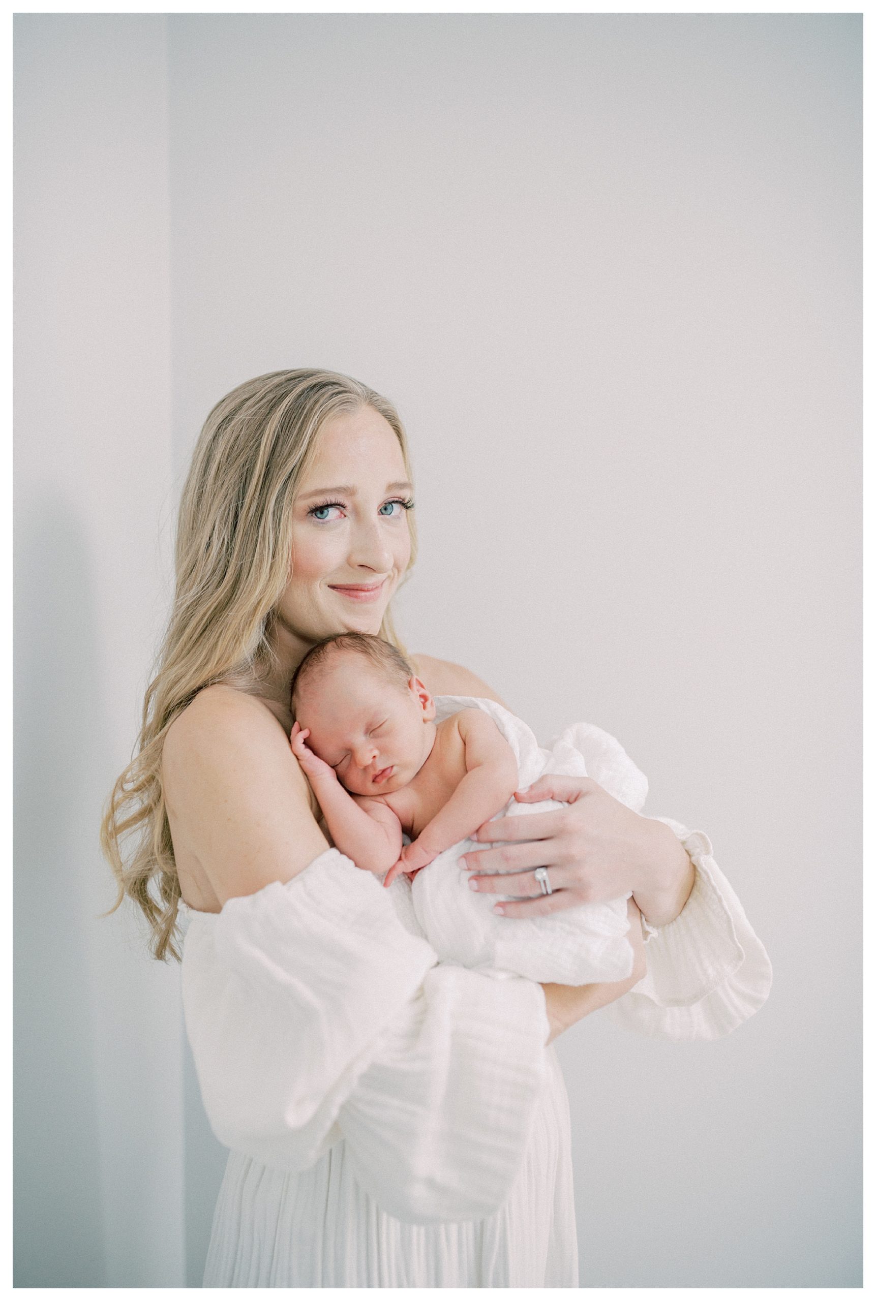 Blonde mother looks at camera as she holds newborn baby up to her chest during DC newborn session.