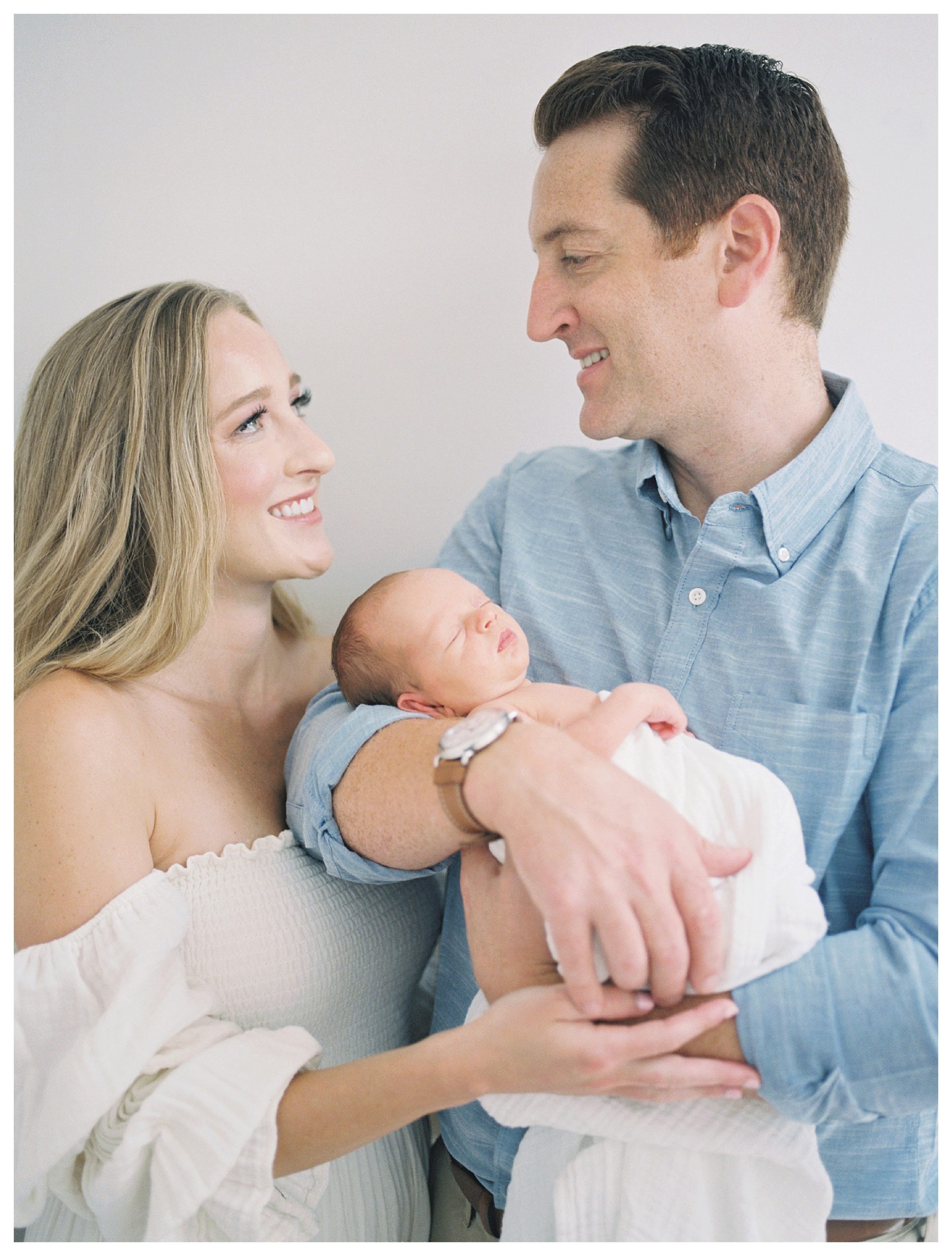New parents look and smile at one another as they hold their newborn baby.