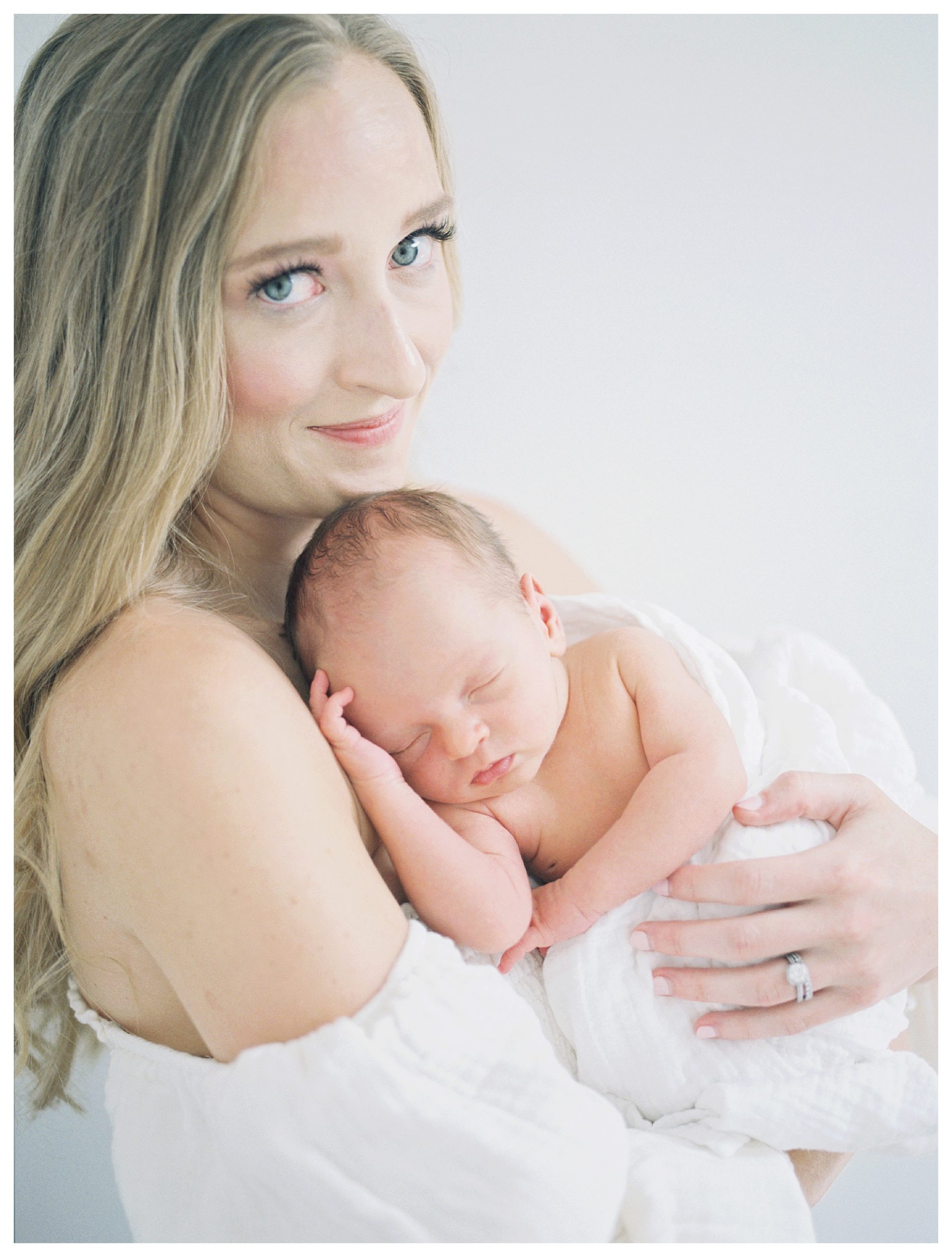 Blonde, blue-eyed mother holds newborn baby up to her chest as she looks at the camera during her DC newborn session on Capital Hill.