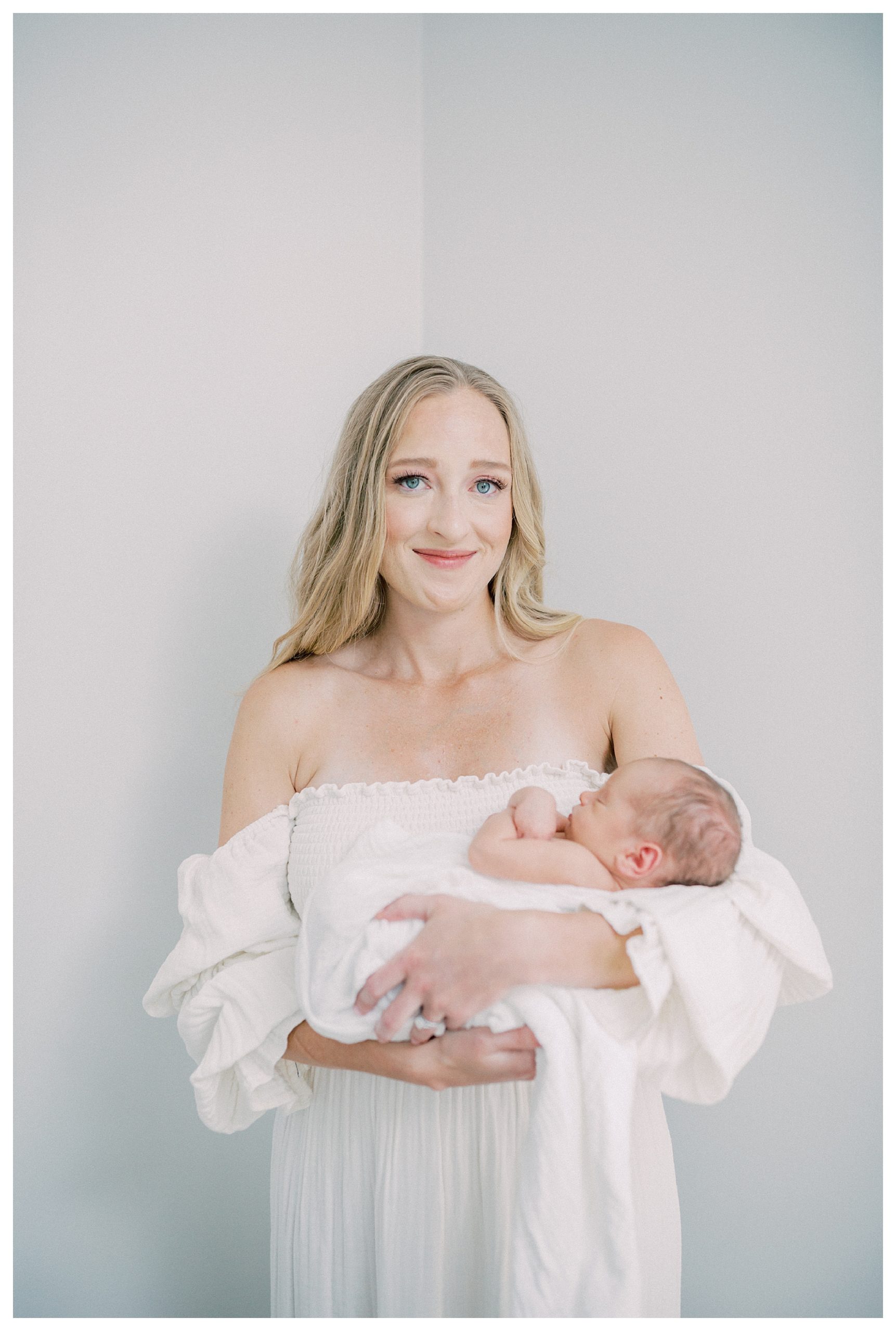 Mother smiles softly while looking at camera, holding newborn son during DC newborn session.