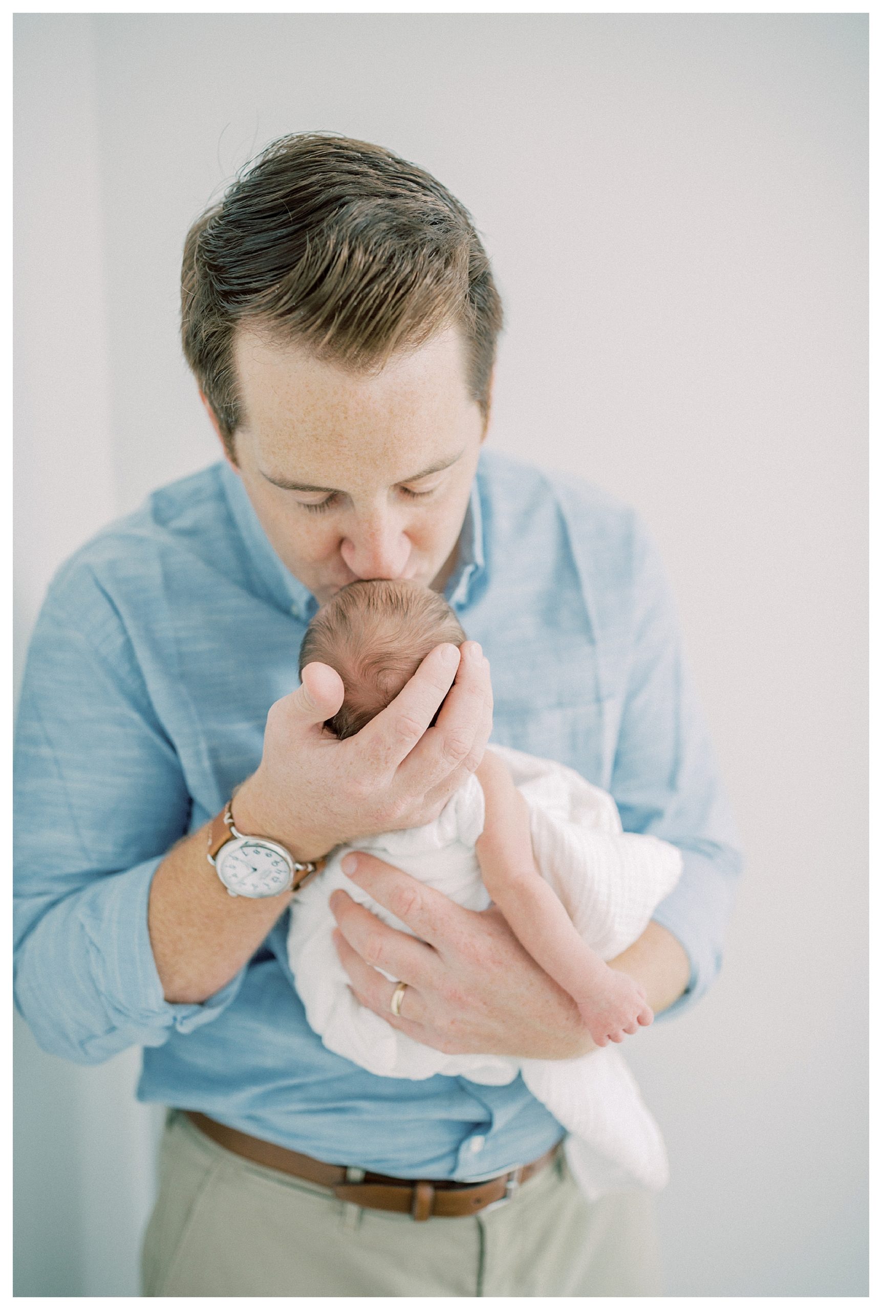 Father leans down and kisses newborn on head during DC newborn session.