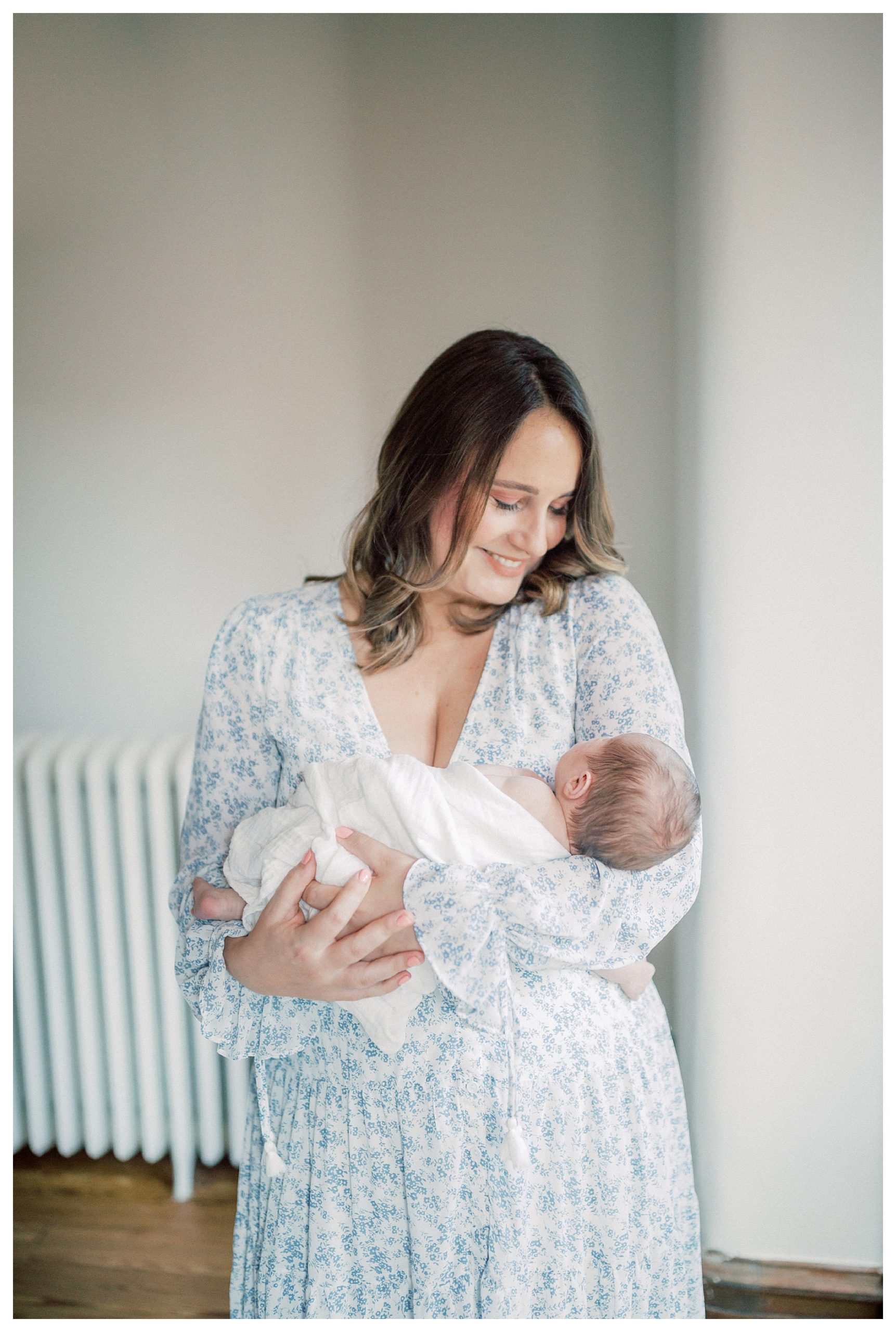Brown-haired mother smiles down at newborn baby during in-home newborn session