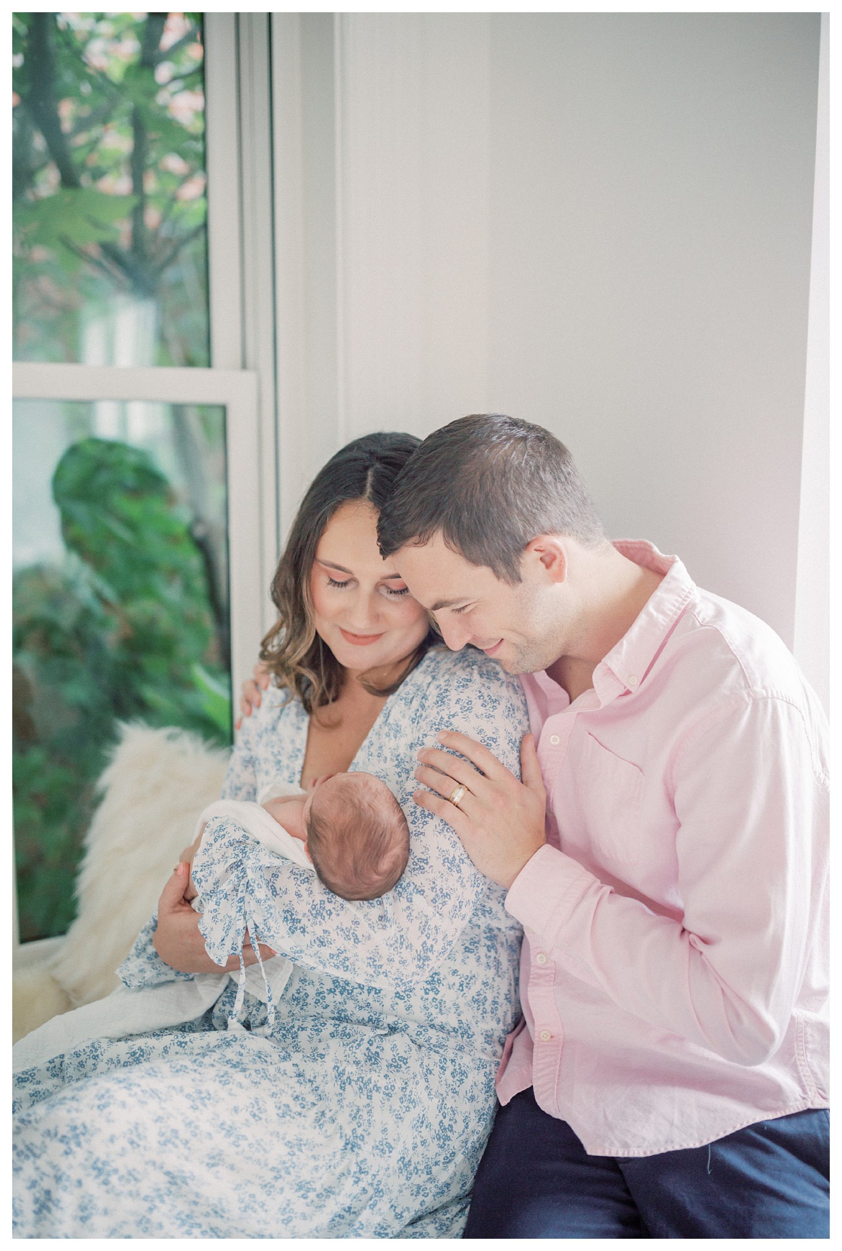 Father leans over his wife's shoulder and smiles at their newborn baby during in-home newborn session.