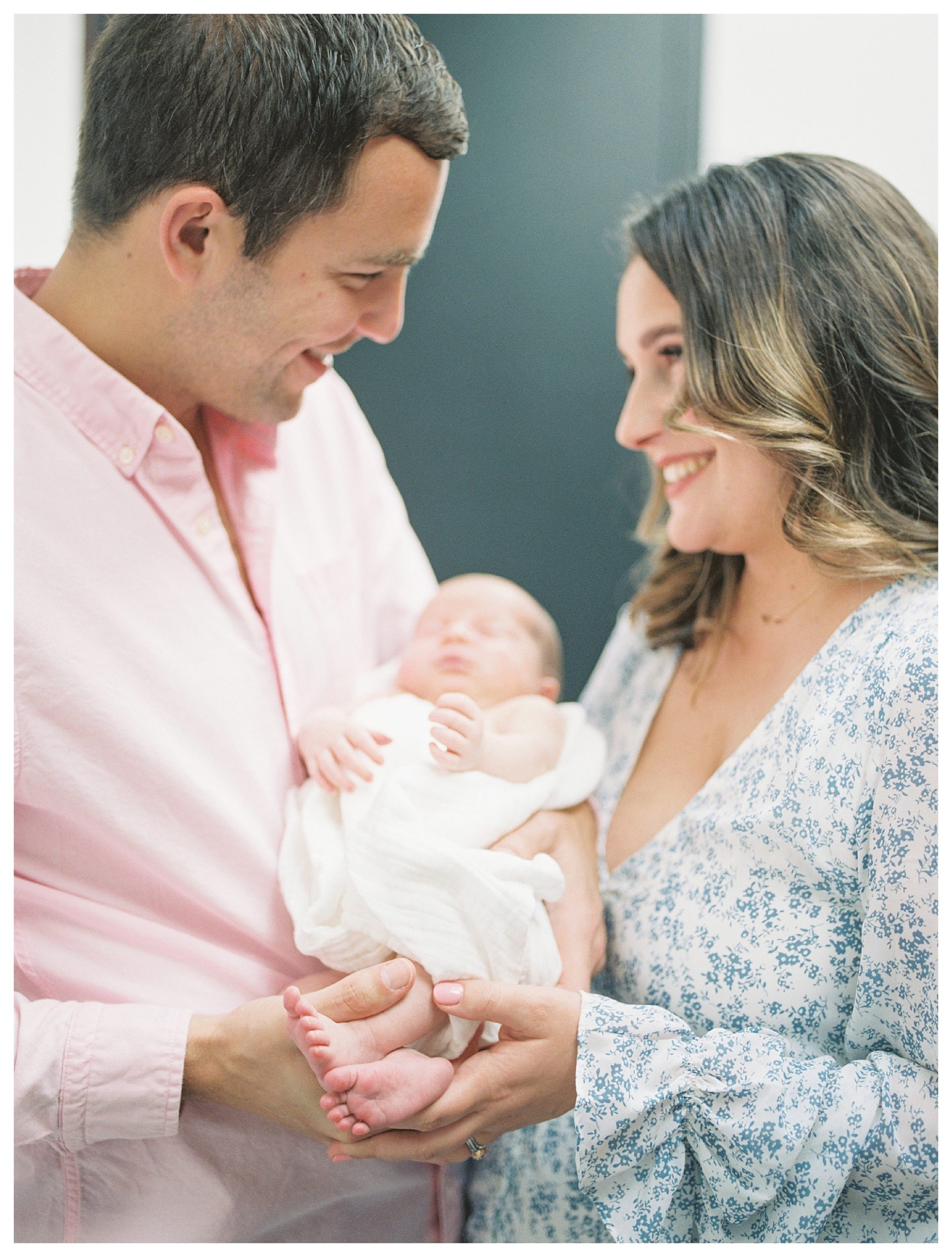 New parents hold their newborn baby and smile at one another during their in-home newborn session.