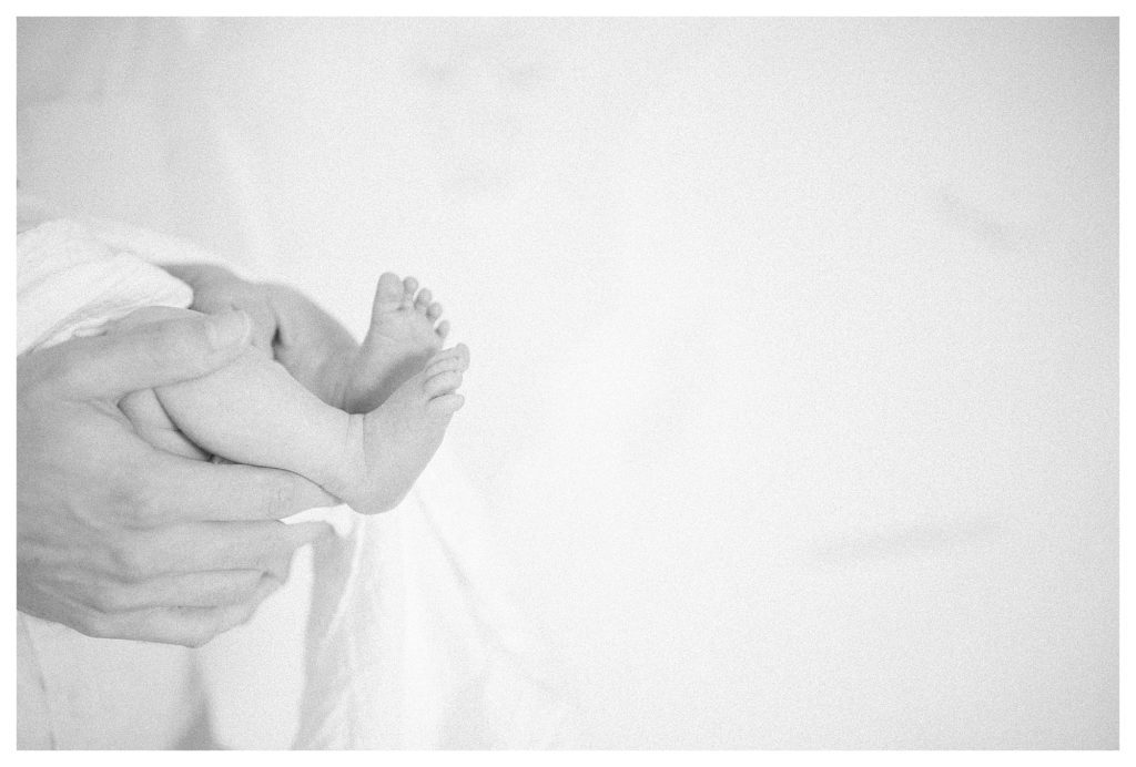 Close-up view of father holding baby's legs during in-home newborn session