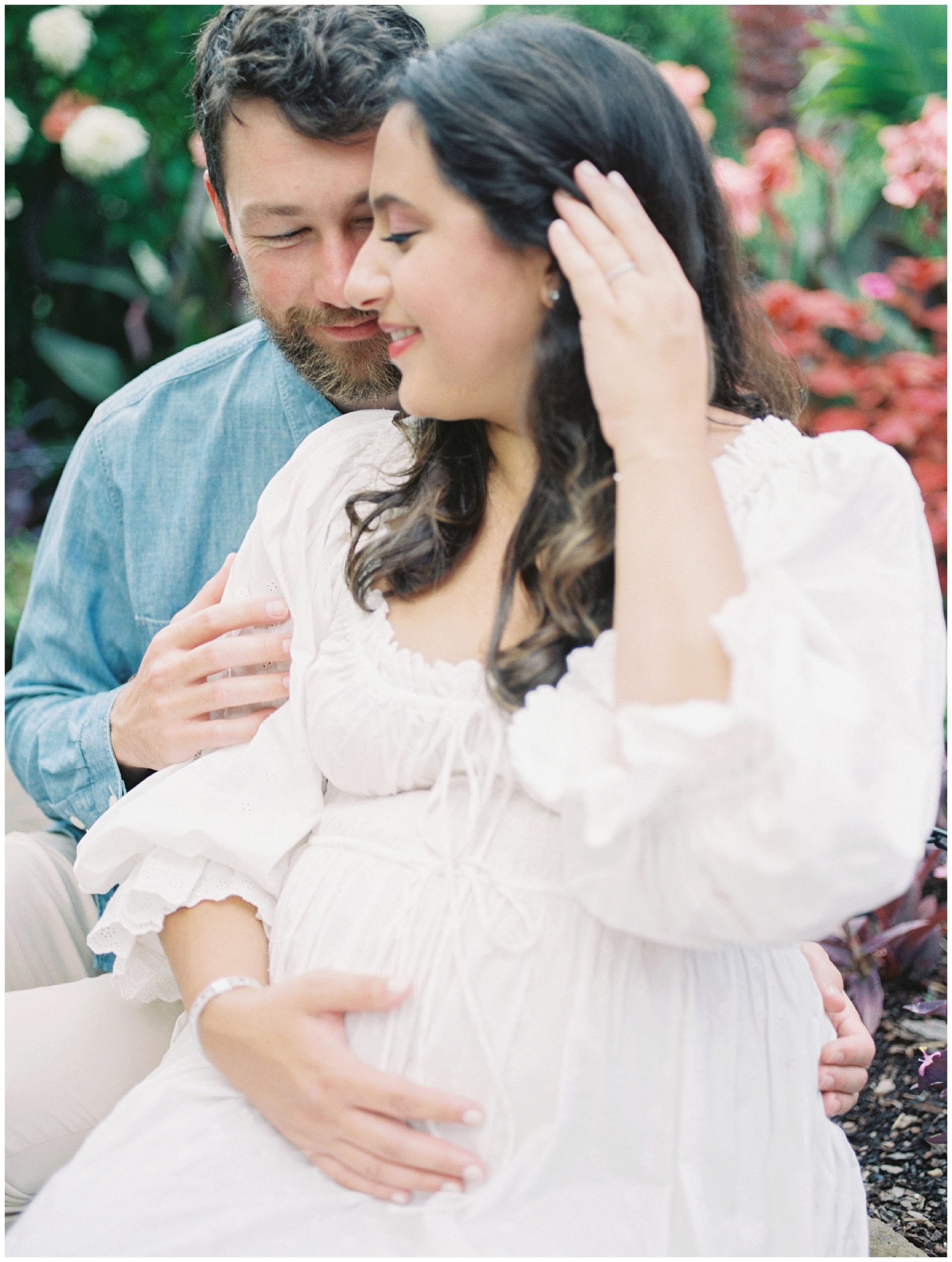 Expecting mother sits with her husband, brushing hair away from her face, during her maternity session.