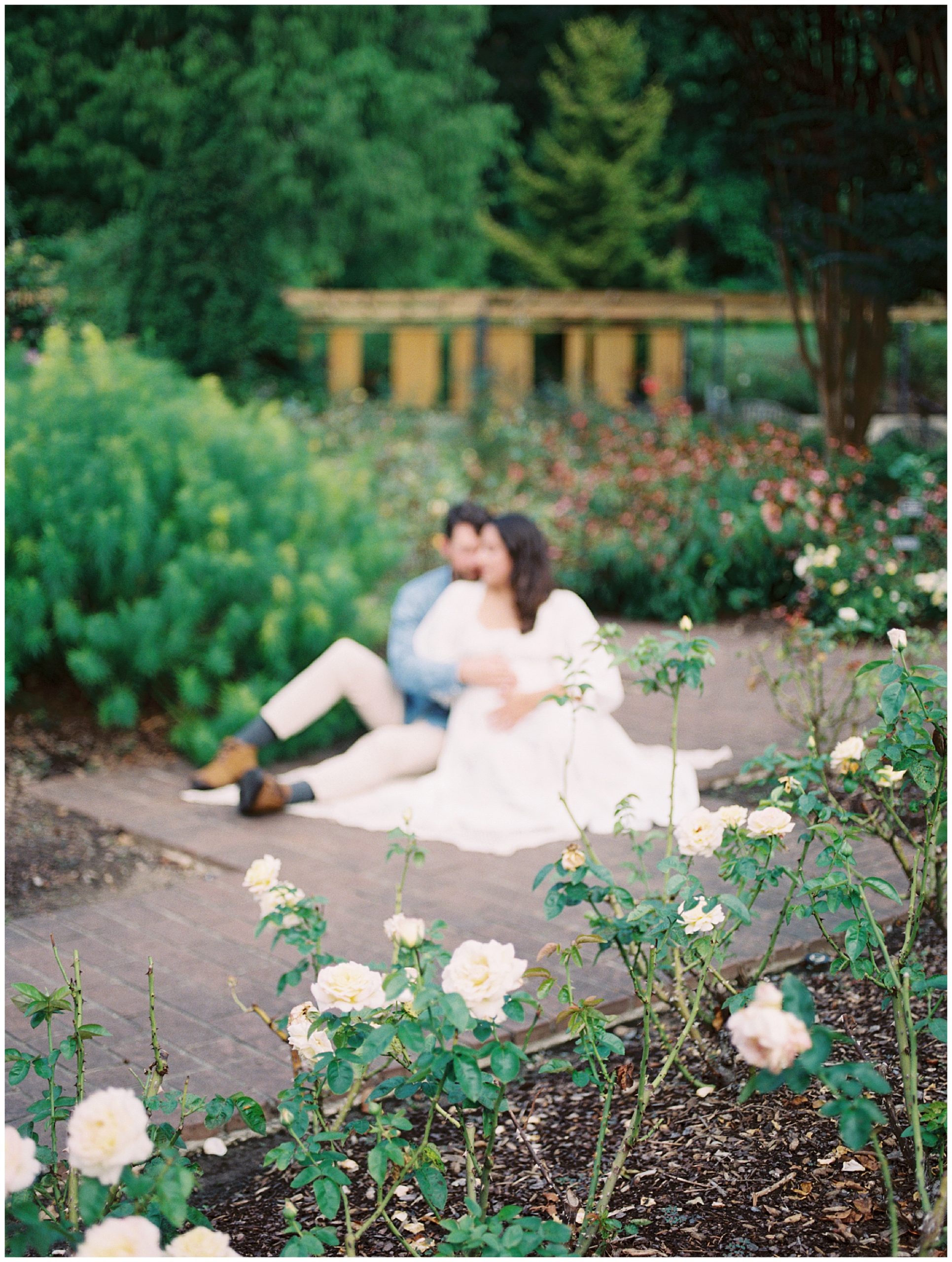 Out of focus image of expecting couple sitting in a garden during their floral maternity session.