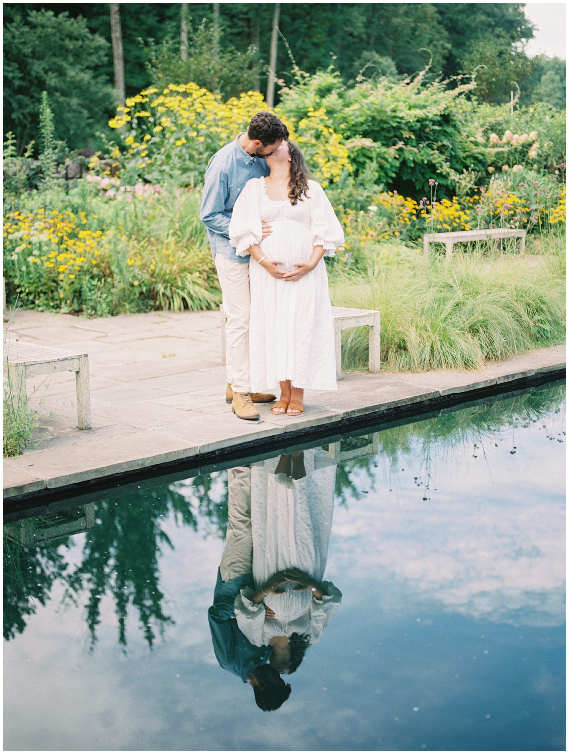 Couple kisses by a pond during their floral maternity session at Brookside Gardens.
