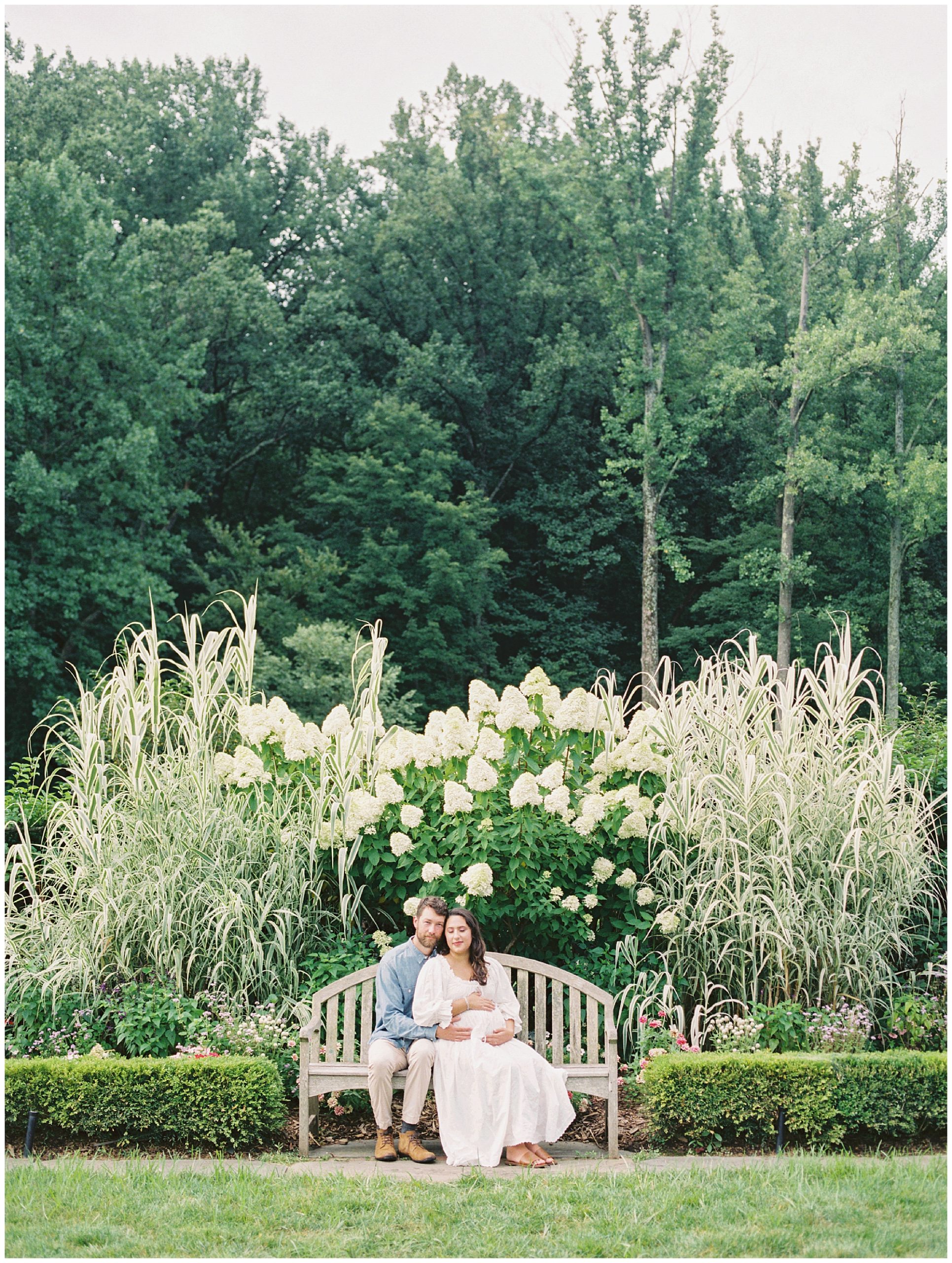 Expecting couple it together on a bench in Brookside Gardens during their maternity session.