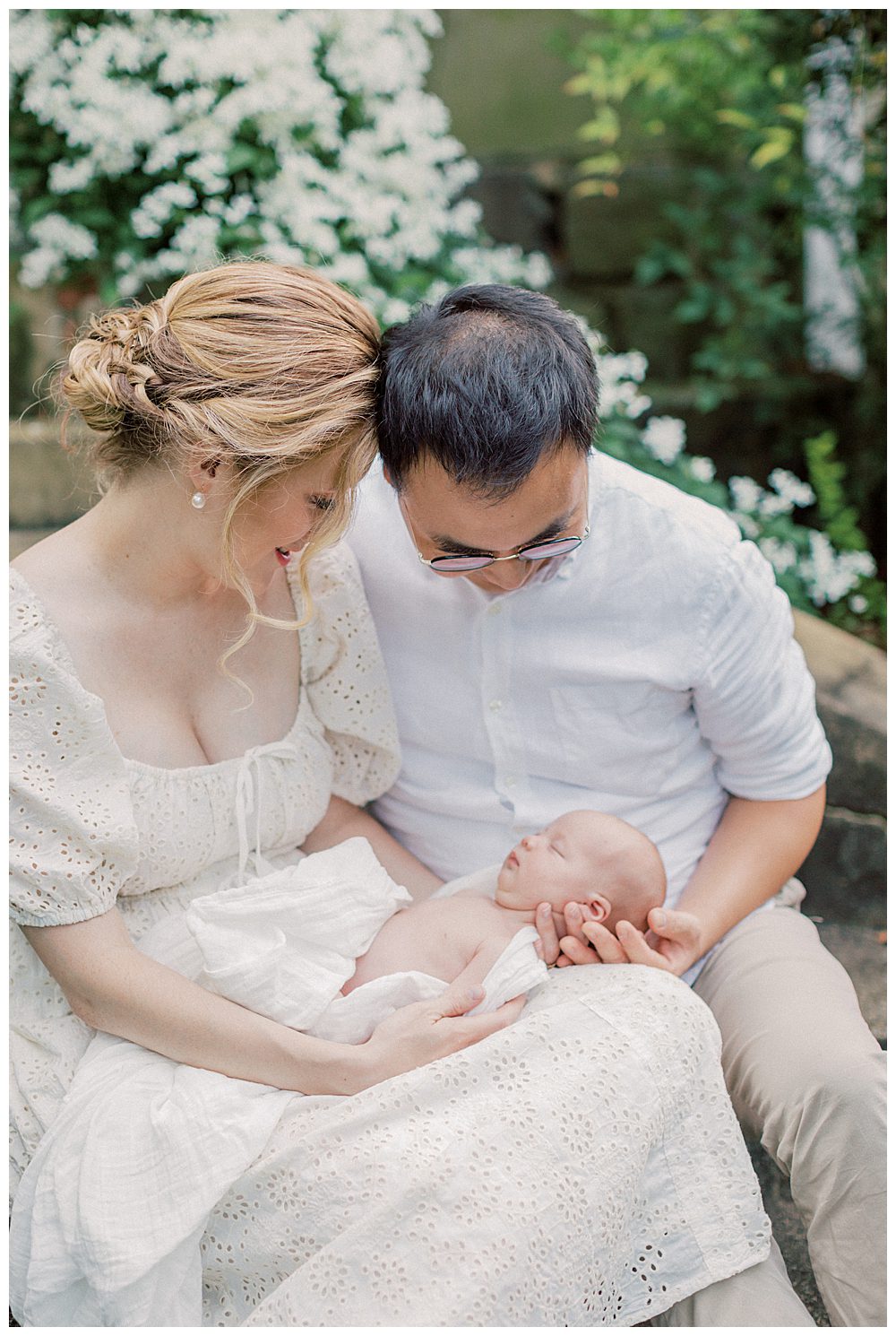 Blonde mother holds newborn daughter while sitting next to husband on steps.