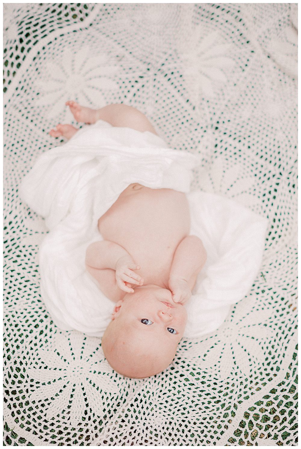 Baby looks up at the camera while laying on white crochet blanket during Alexandria VA newborn session.