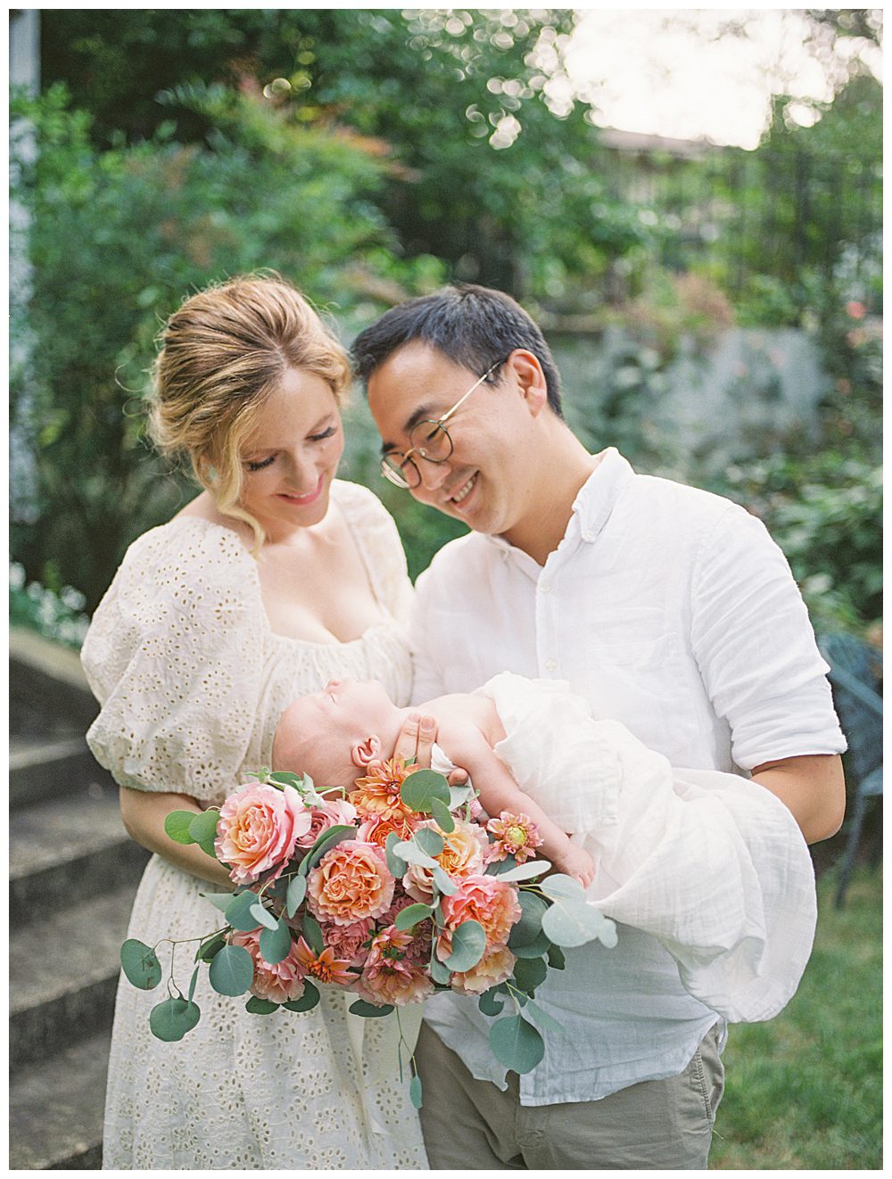 New parents hold newborn baby with bouquet of roses during their Alexandria VA newborn session in a garden.