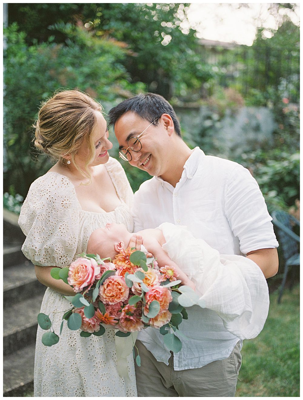 Mother smiles at her husband while they hold their newborn baby girl on bouquet of roses during Alexandria VA newborn session.