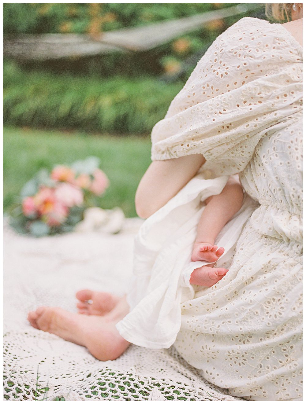 Tiny baby toes peek from behind mother while baby is held in a garden.