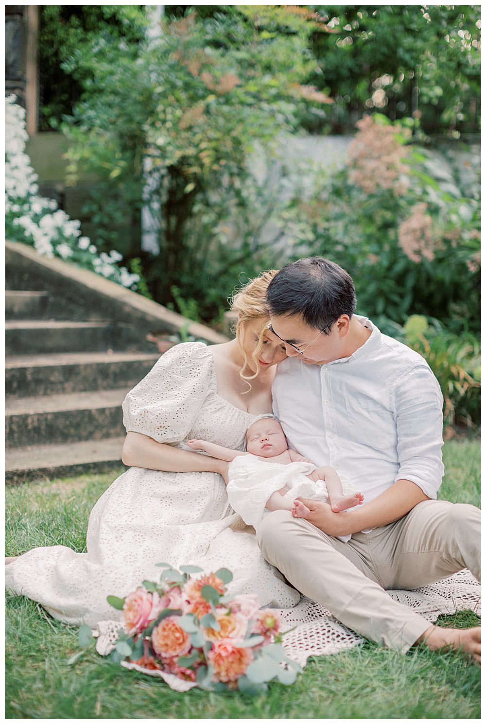 Mother leans into her husband as they hold their newborn baby during Alexandria VA newborn session in a garden.