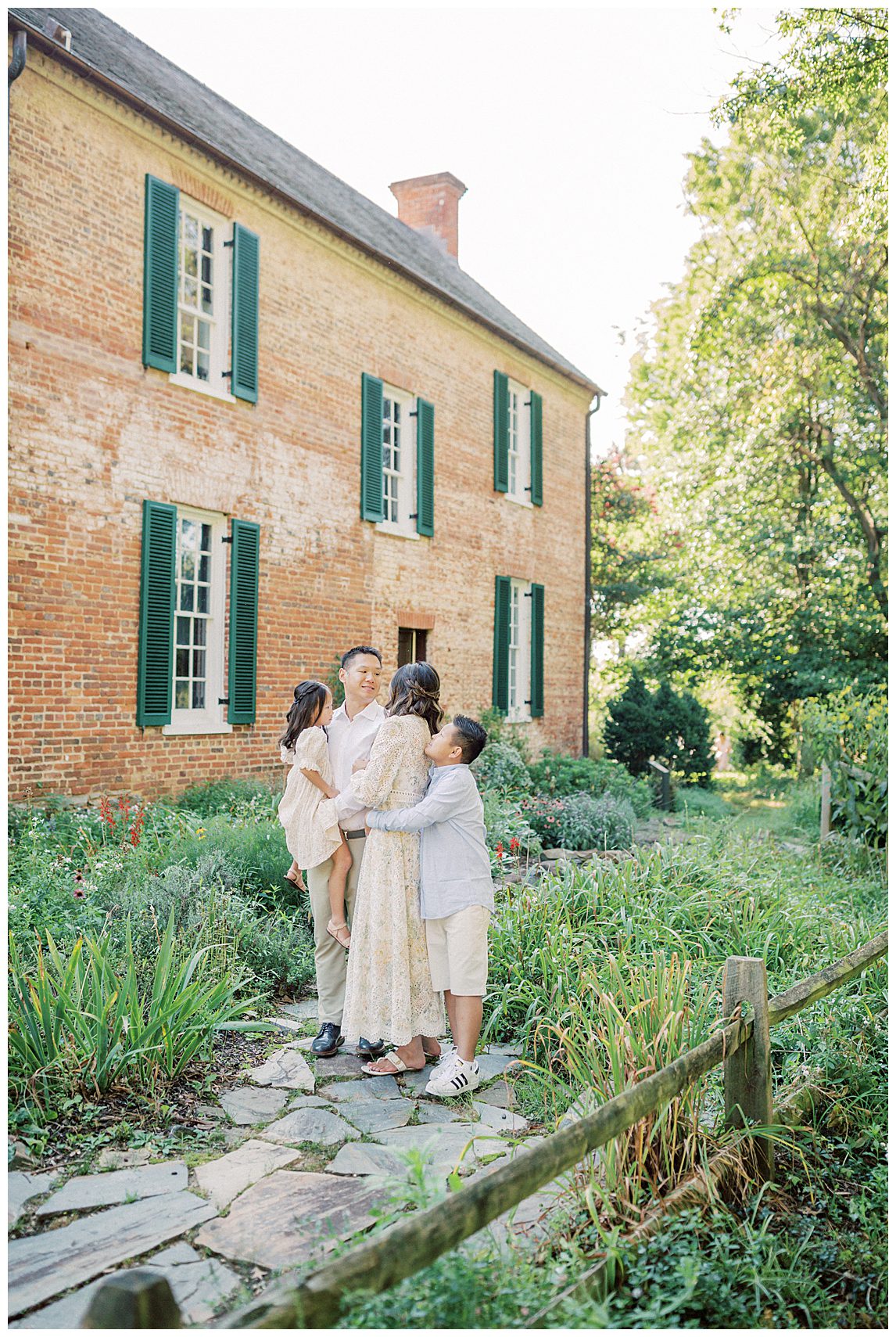 Family stands in front of brick house at Colvin Run Mill during their family photo session.