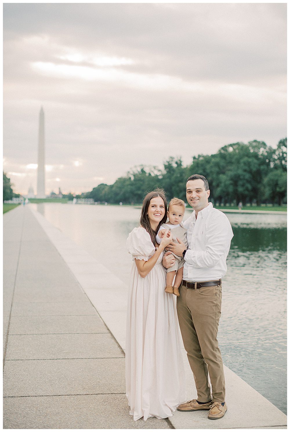 Parents hold toddler son by DC reflection pool during DC Monuments Family Photo Session.