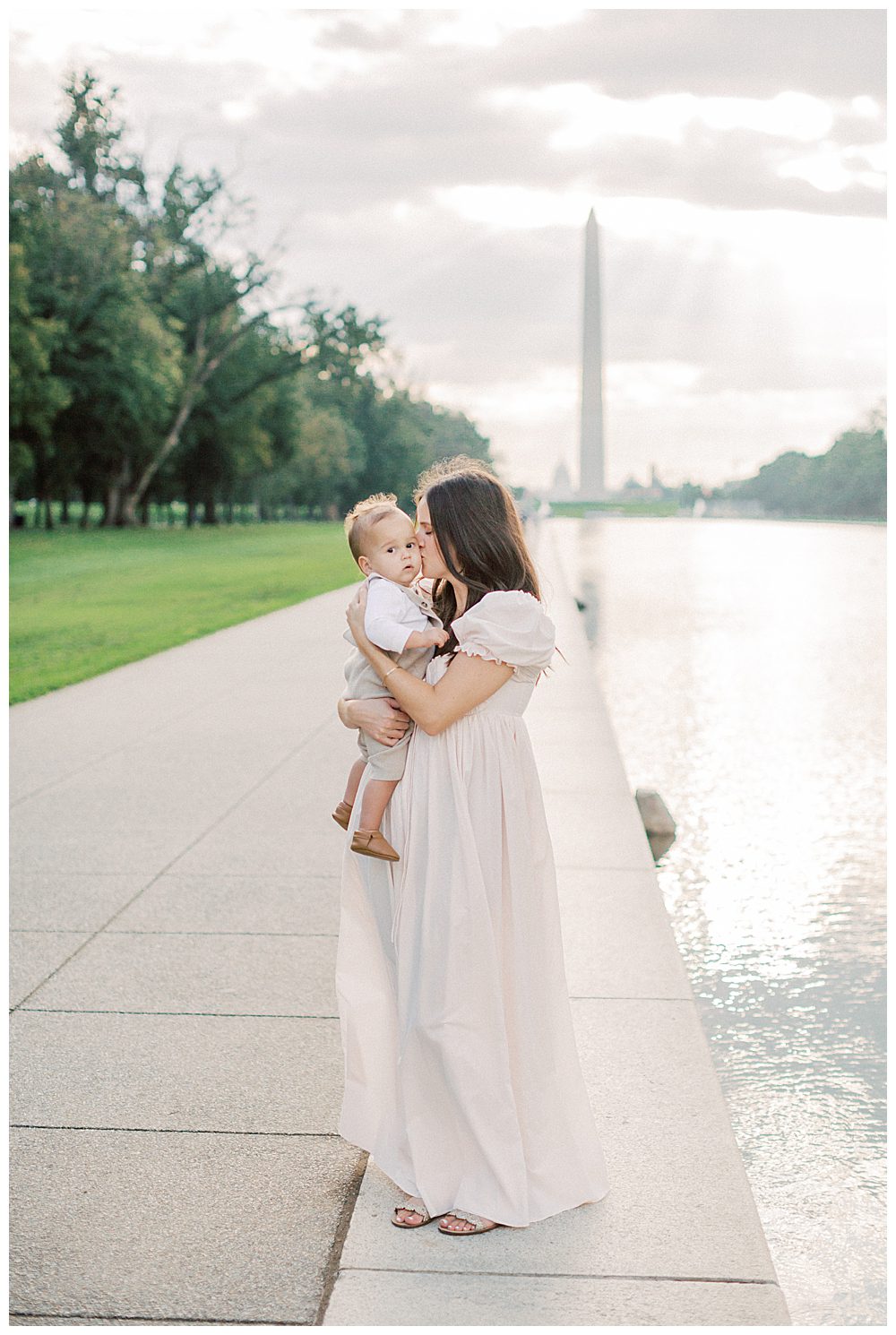 Mother kisses her toddler's cheek as she stands by the DC reflection pool during DC Monuments Family Photo Session.