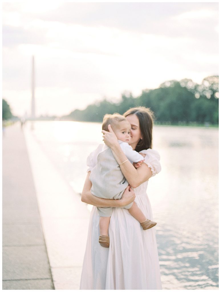 Mother holds baby boy close to her as she stands near reflecting pool in DC.
