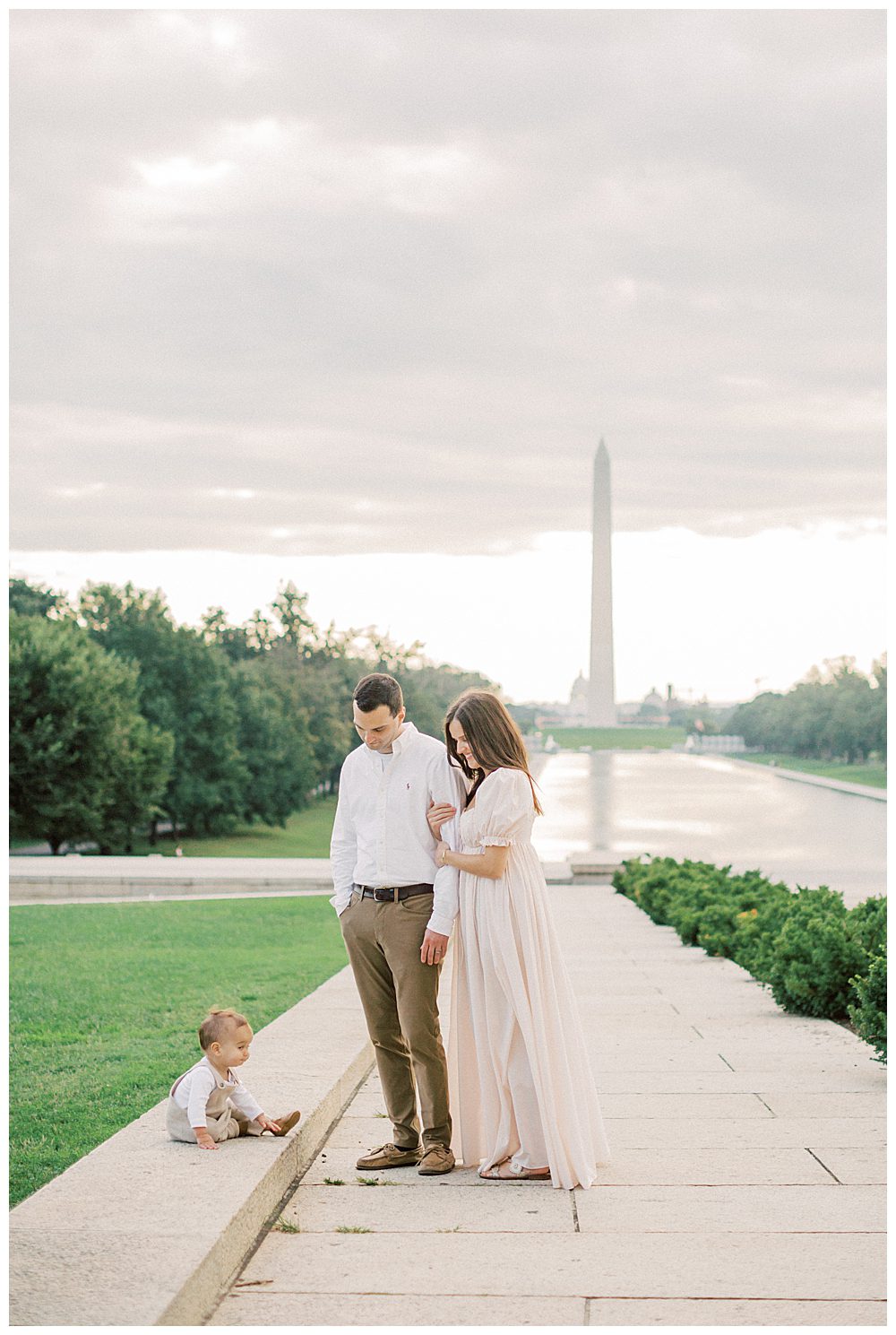 Mother and father stand in front of Washington monument smiling down at their toddler son.