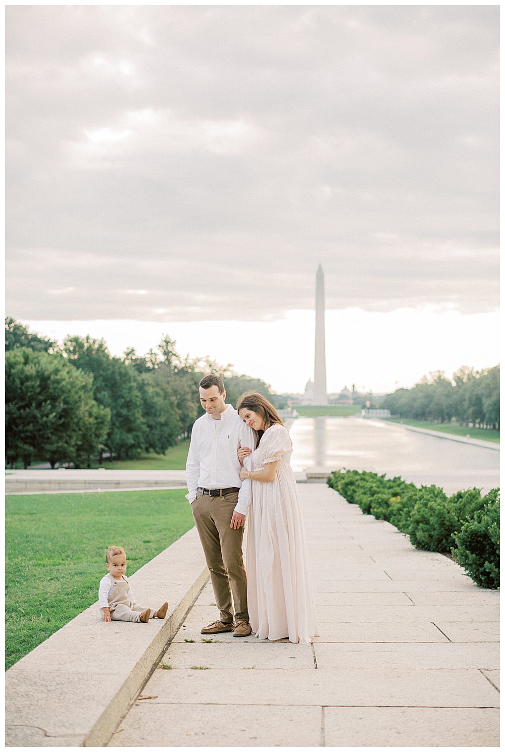 Parents stand in front of Washington Monument and smile down at toddler son during DC Monuments Family Photo Session.