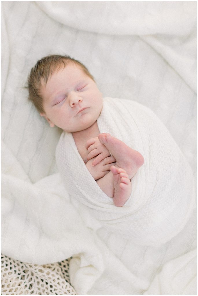 Newborn baby girl swaddled in white and laying on knit blanket during Great Falls newborn session.