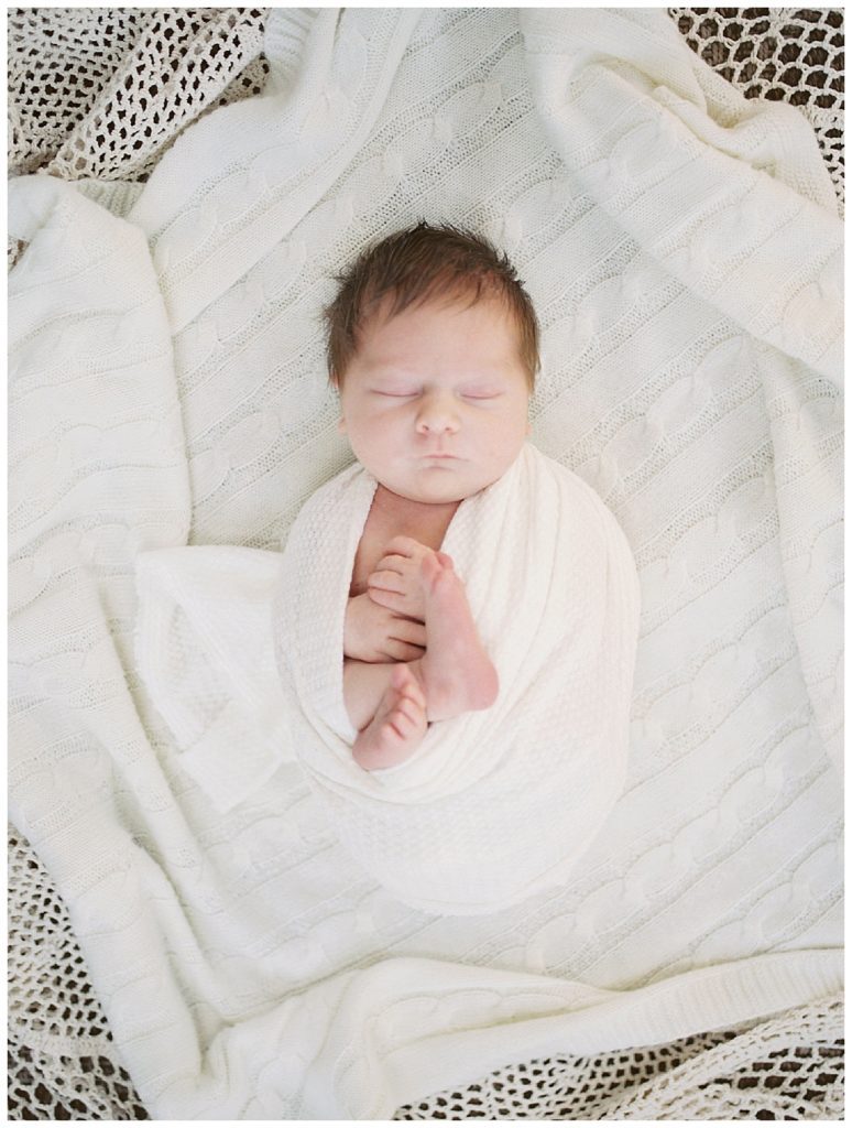 Newborn baby girl swaddled in white sleeps on knit blanket during Great Falls newborn session.