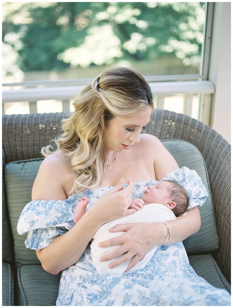 New mother holds her baby girl's hand while holding her newborn baby in her arms.