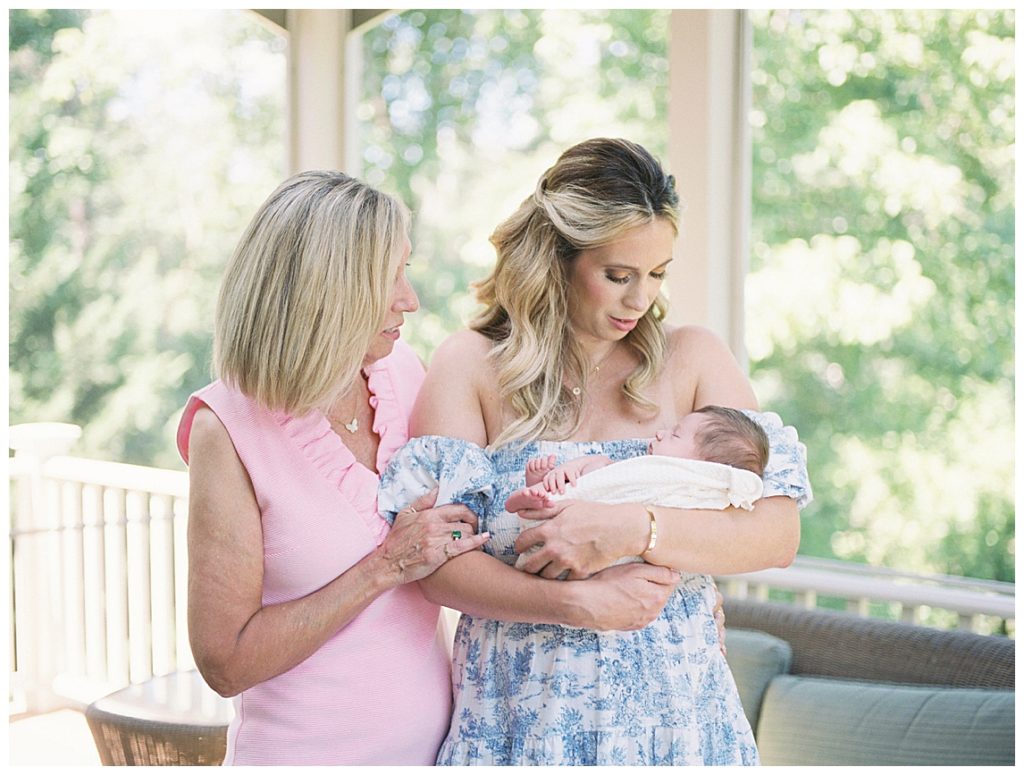 Blonde mother holds her newborn baby with her mother standing next to her.
